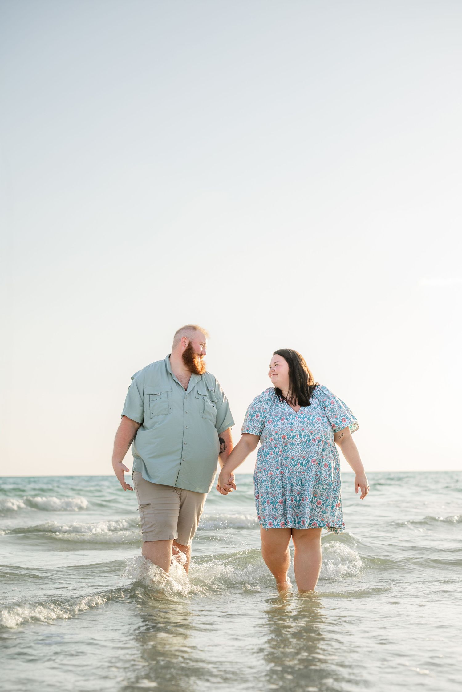 Playful couple holding hands while walking through ocean surf at sunset.