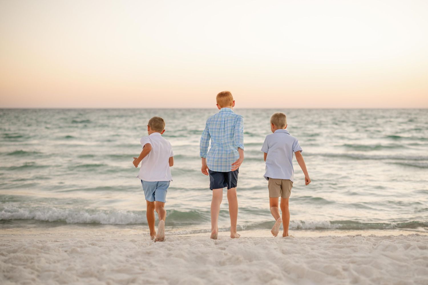 Three people walking along the shoreline at sunset with waves rolling in.