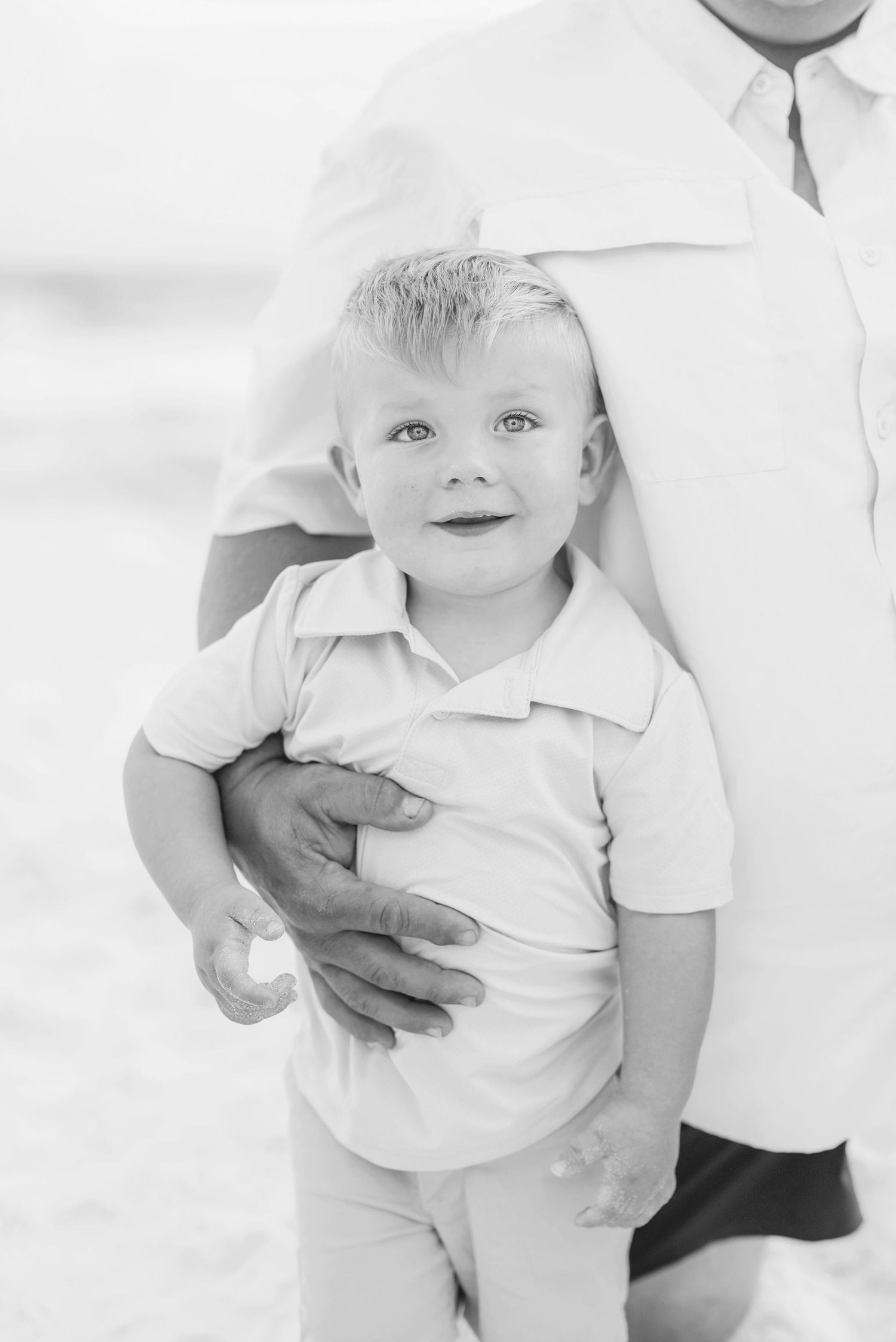 Black and white portrait of parent holding young child in white attire.