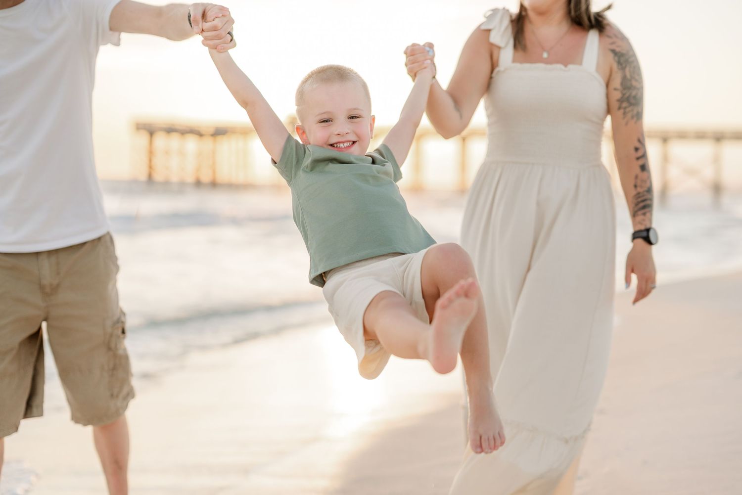 Parents swinging child between them while walking on beach at sunset.