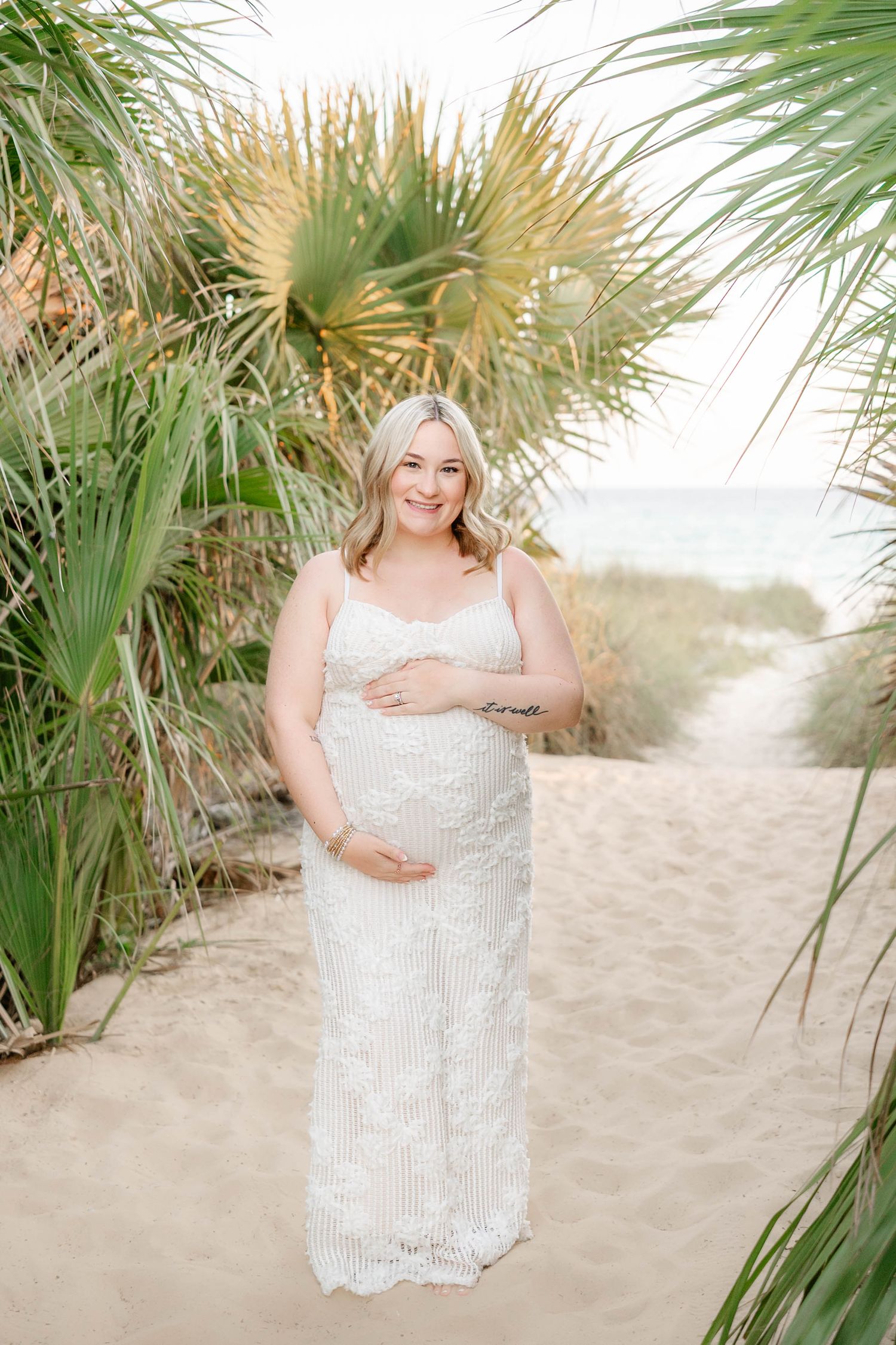 Maternity photo of woman in sequined dress among tropical palm fronds on beach in Panama City Beach, Fl..