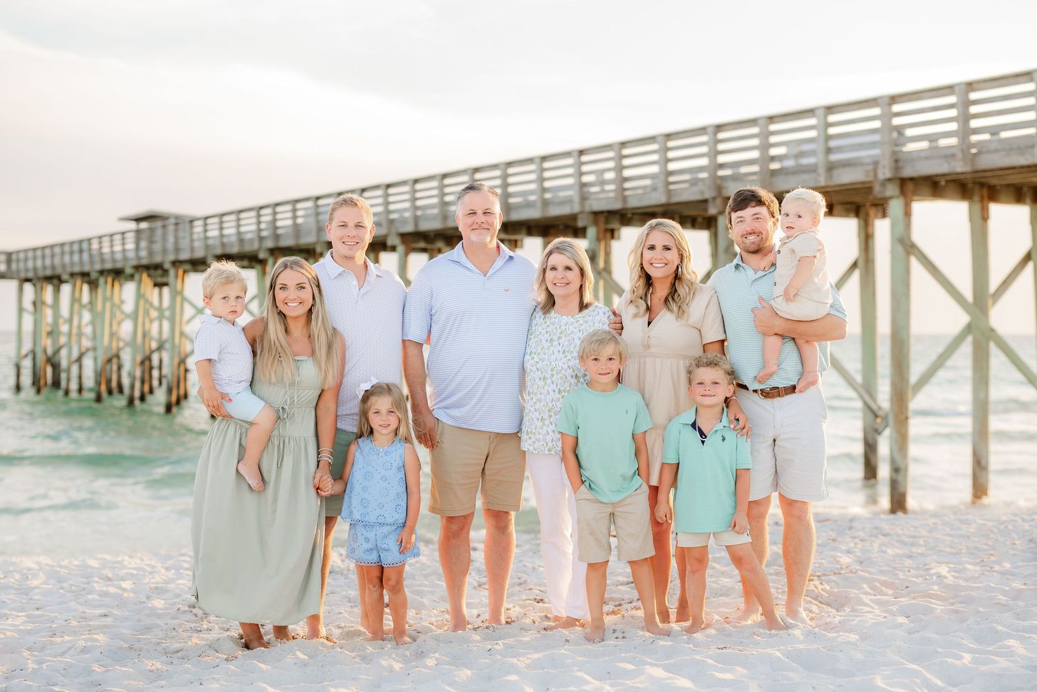 Family beach portraits in coordinating pastel outfits near oceanfront pier.