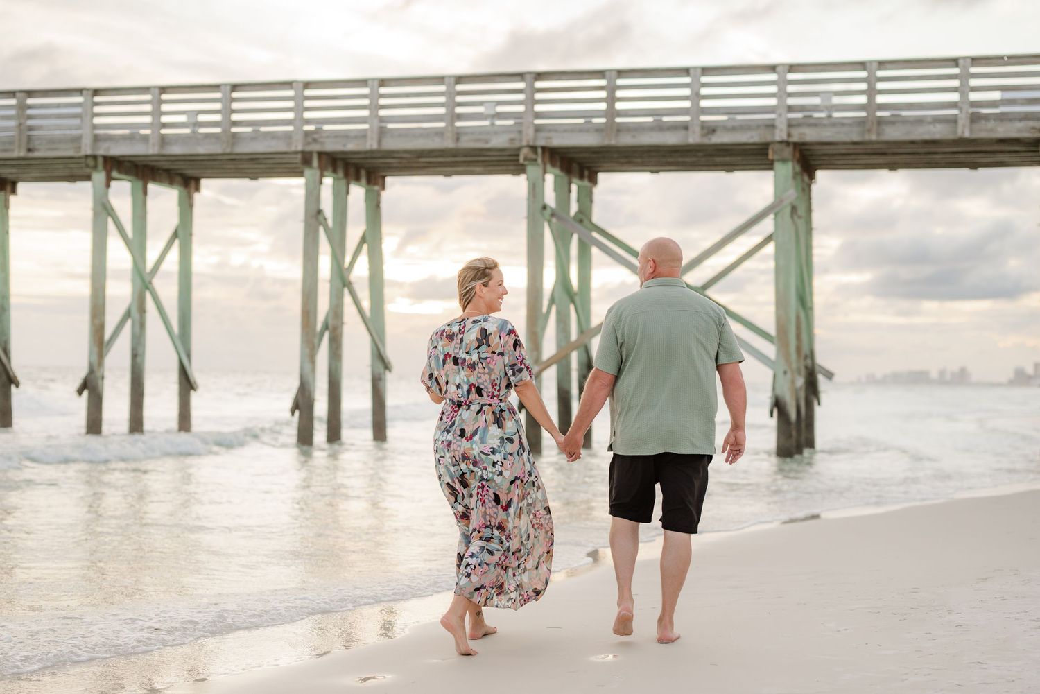 People walking along beach pier during golden hour with ocean waves in background.
