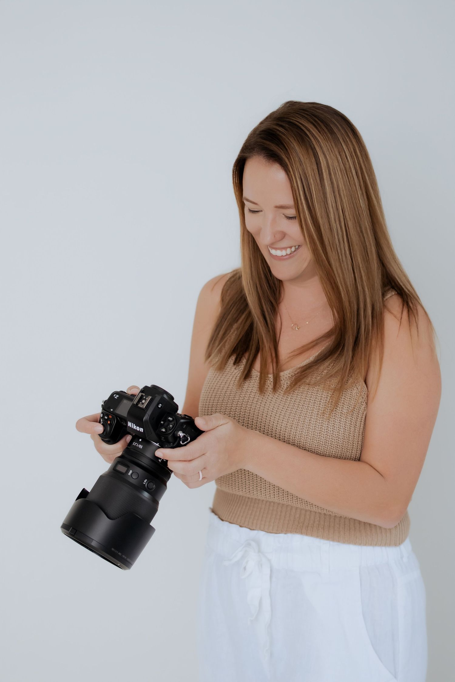 Photographer in beige sweater reviewing images on a professional camera against white background.