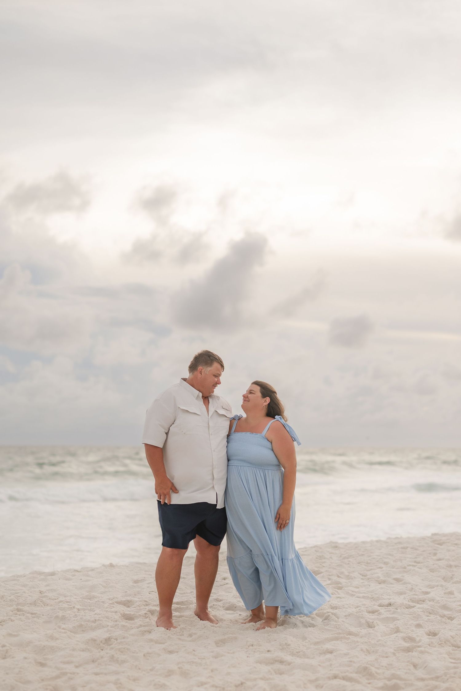 Couple sharing intimate moment on white sandy beach during cloudy sunset.