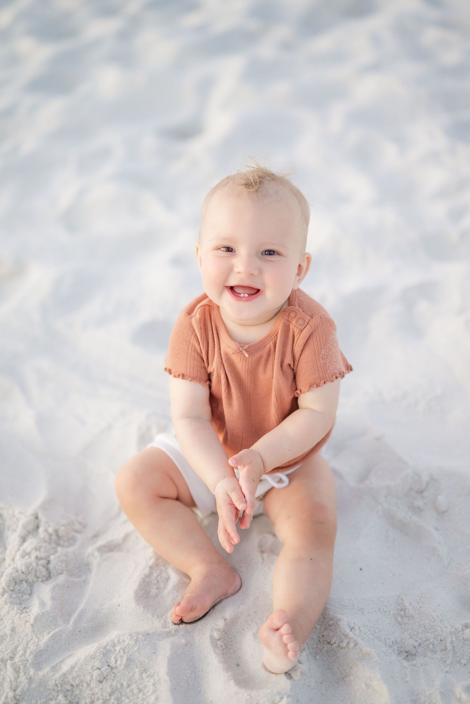Baby in peach colored outfit sitting on pristine white sand beach in Panama City Beach, Fl..