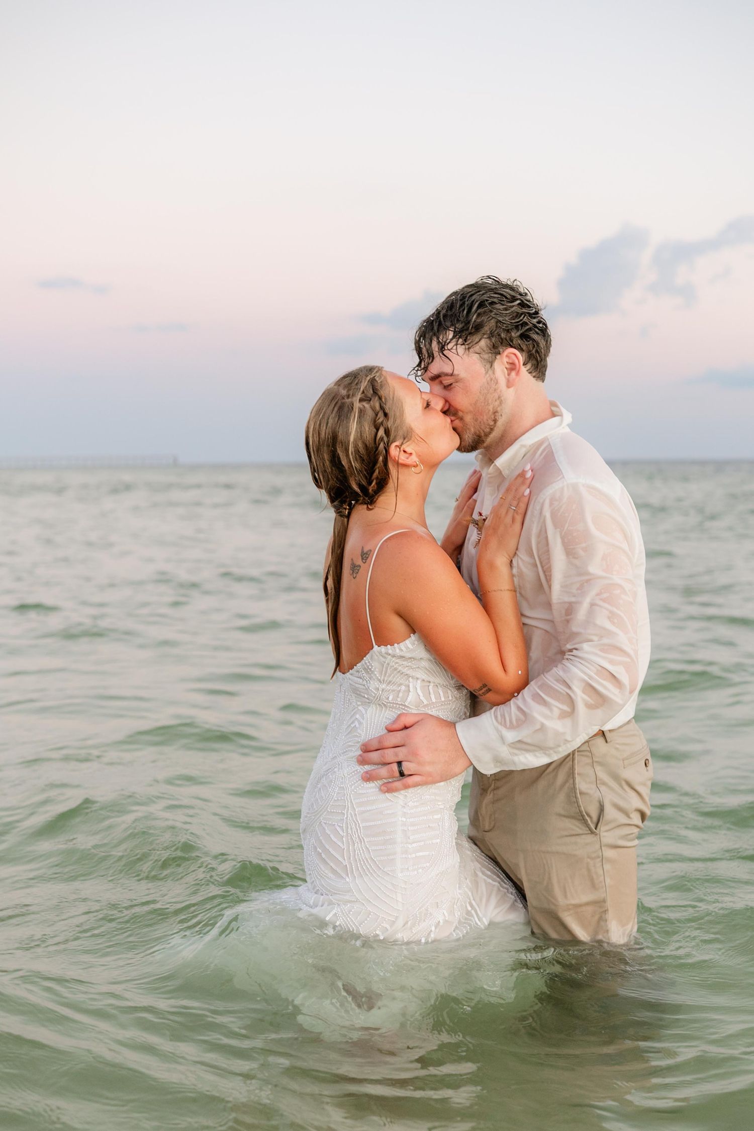 Couple shares intimate moment while wading in ocean waters at dusk.