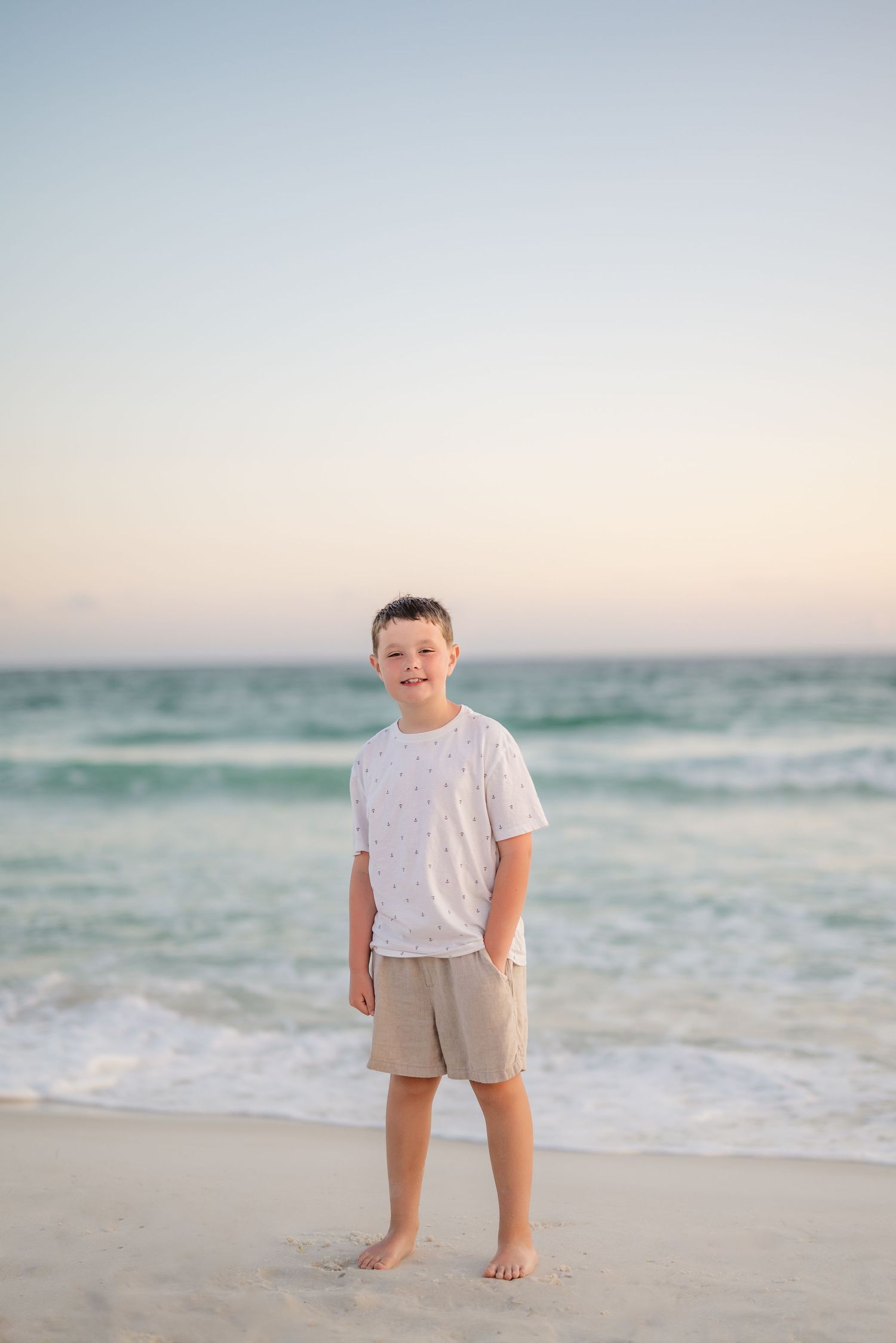 Child in casual summer outfit standing on white sand beach at dusk in Panama City Beach, Fl..