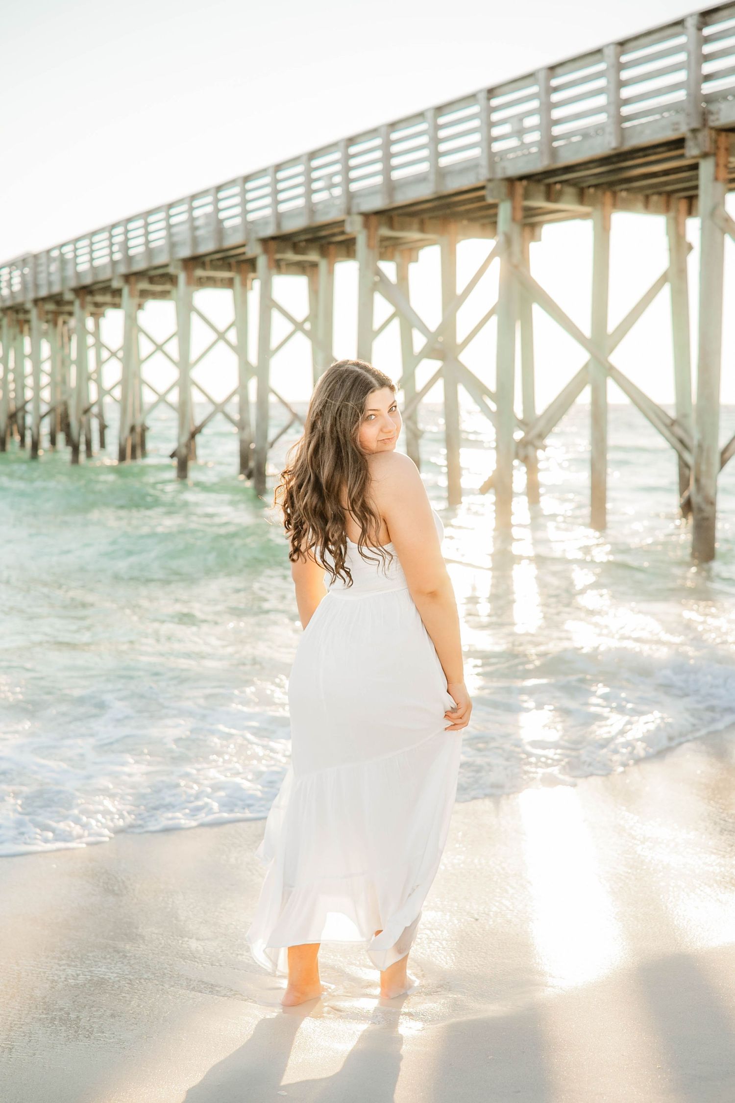 Dancing and twirling on the beach with a wooden pier and ocean waves in the background.