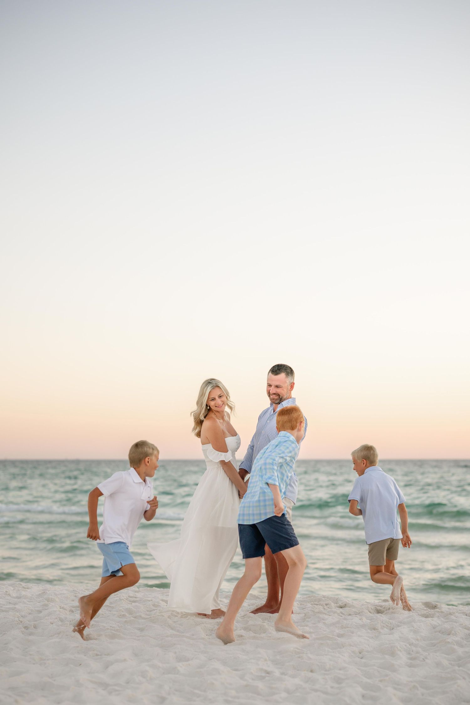 A family plays and jumps together on a beach during golden hour.