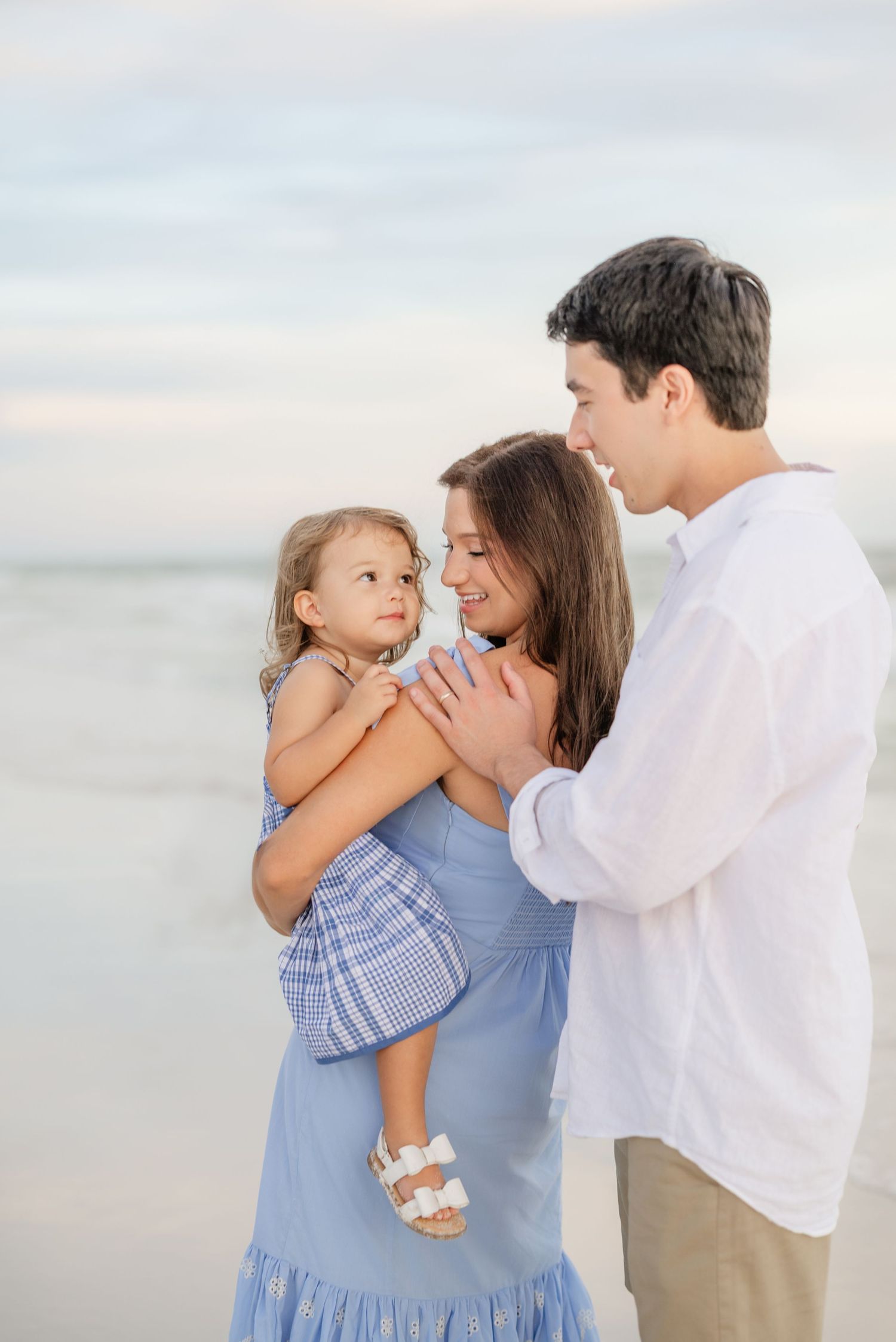 Family of three in coordinating blue and white outfits share intimate moments on the beach.