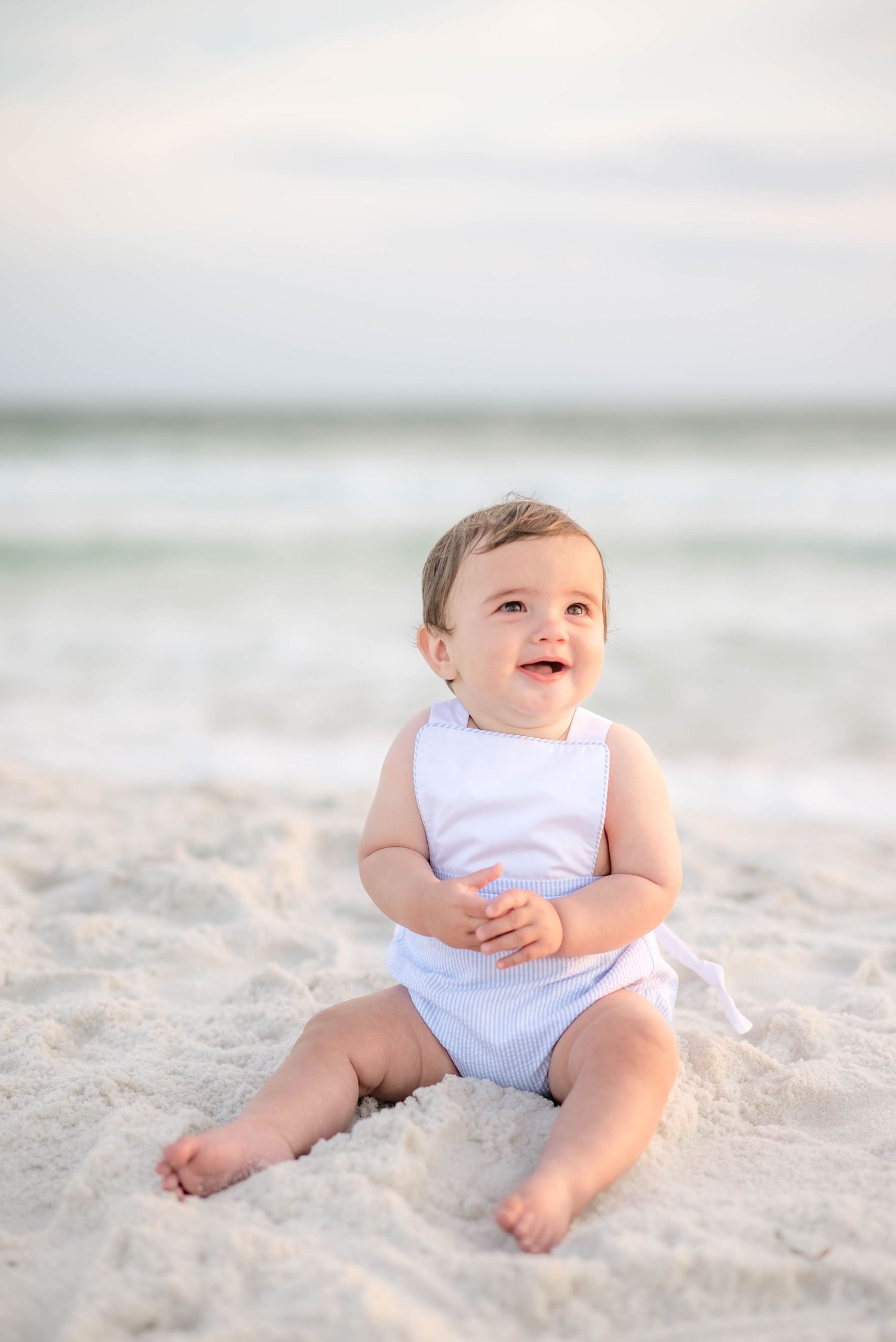 Baby sitting on white sand beach wearing light blue outfit. in Panama City Beach, Fl.