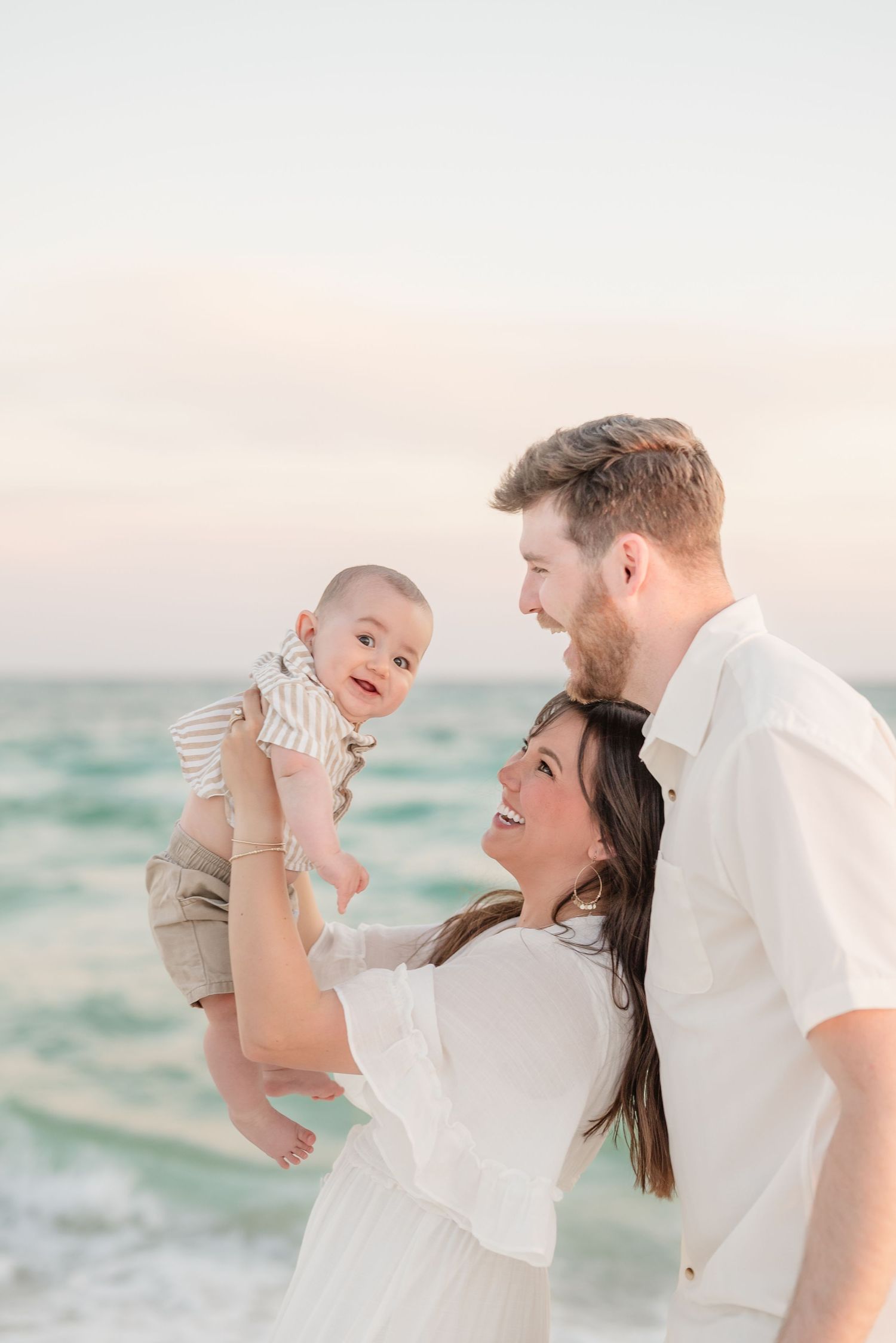 Family sharing tender moments on a beach with turquoise waters at sunset.
