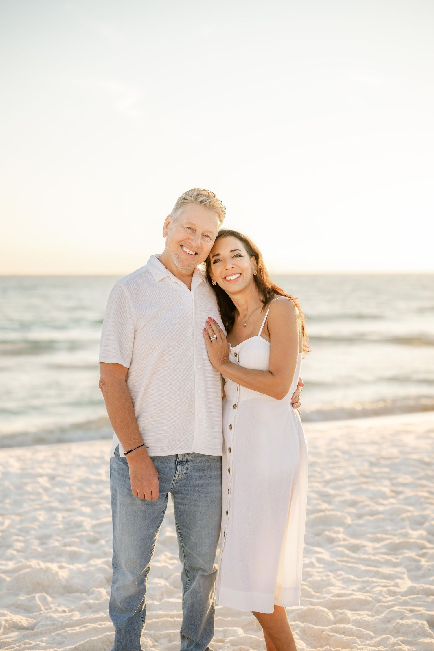 A couple shares a tender moment while posing for photos on a sunny beach.