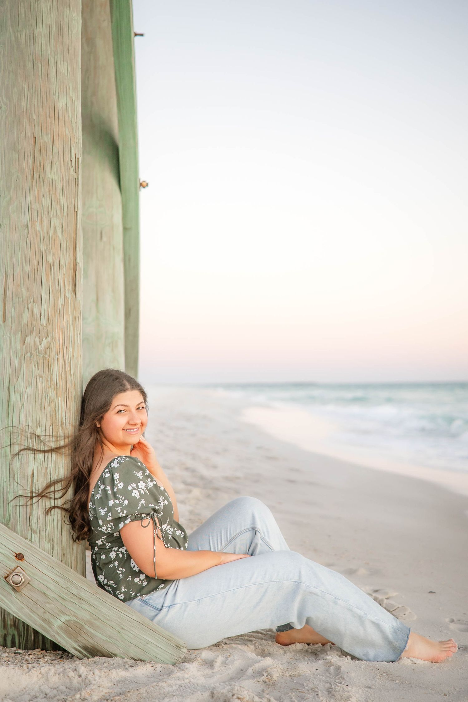Relaxed beach portraits with a wooden pier post and soft sunset lighting.