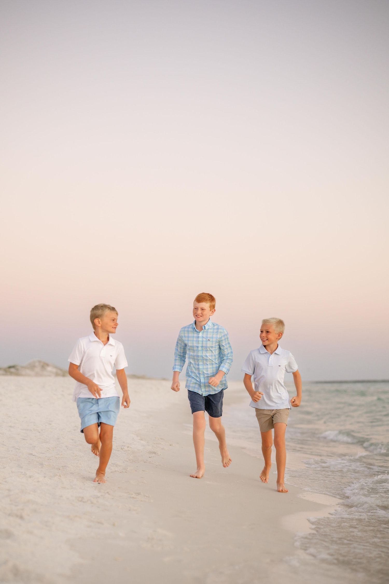 Three children run and play along the beach shoreline at sunset.