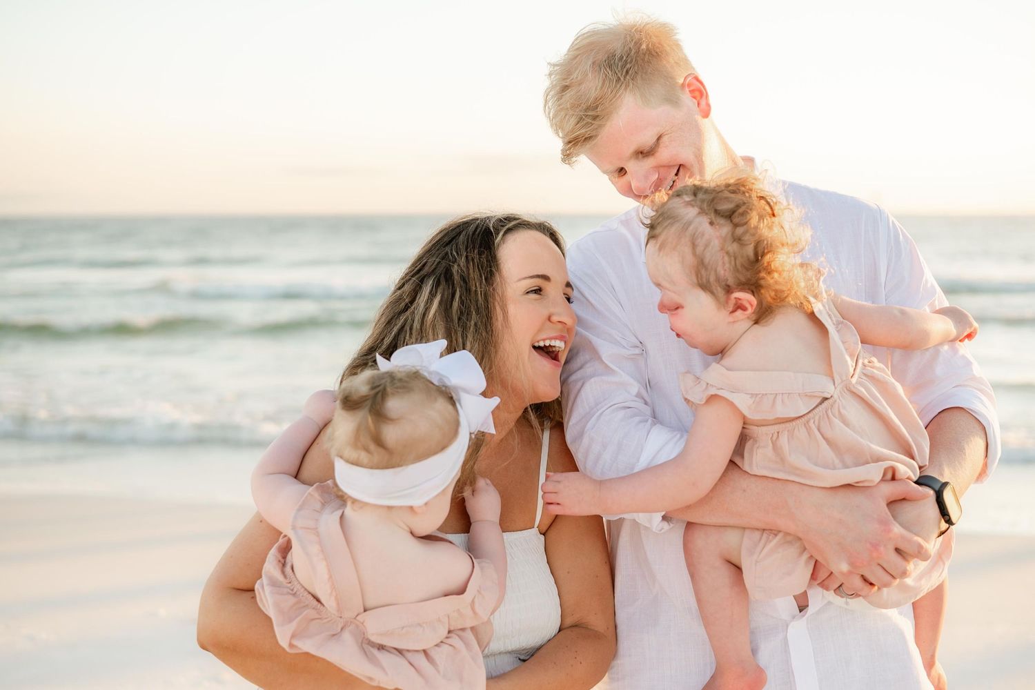 Joyful family laughing and playing during beachside photo session at sunset.