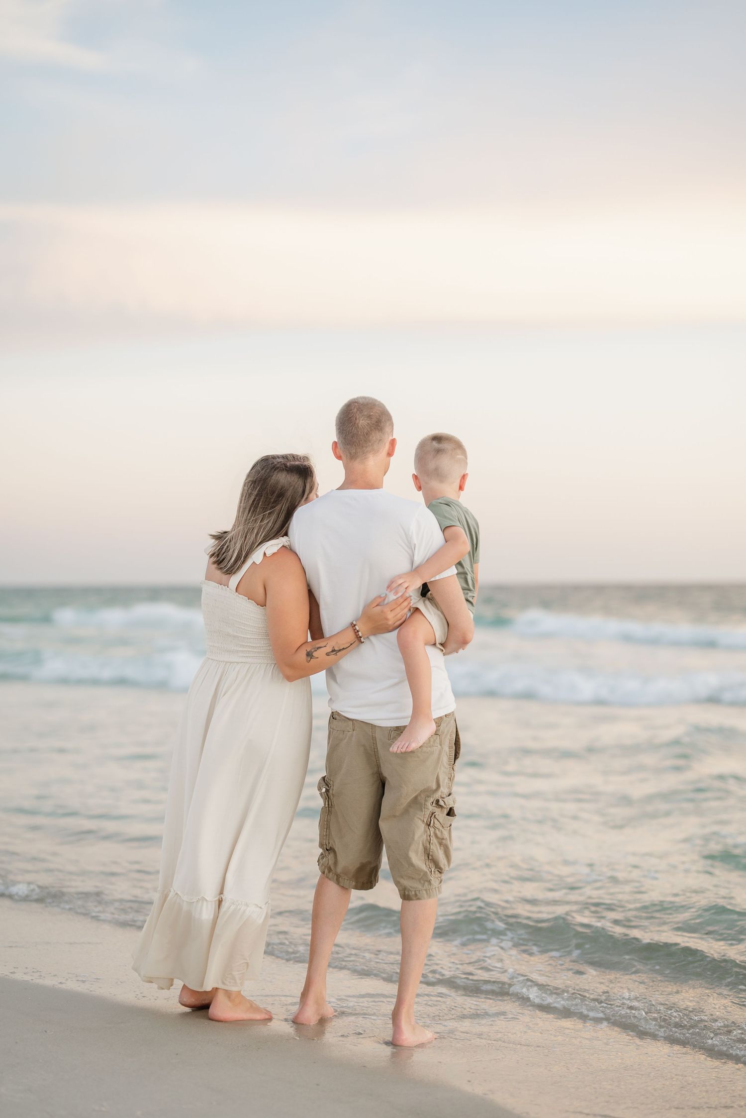 A family stands together watching the ocean waves at sunset.