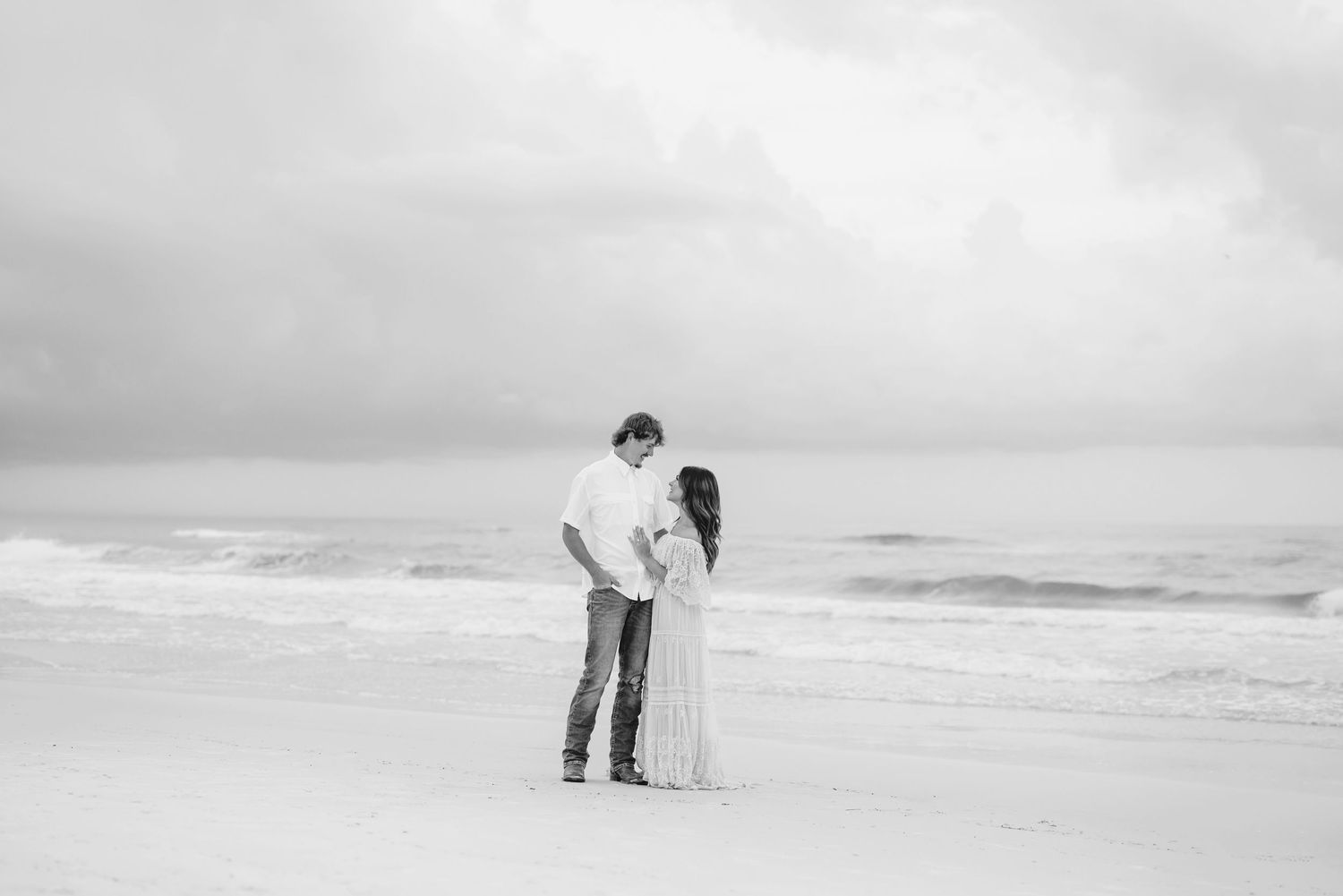 Minimalist beach photography with distant couple silhouetted against cloudy sky.