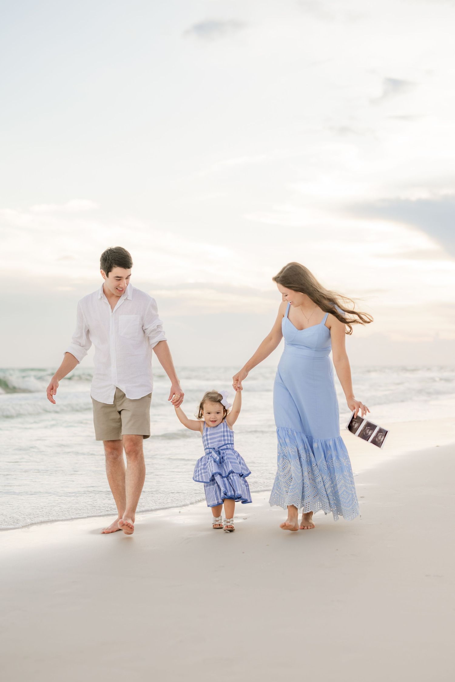 Family walking hand in hand along shoreline during golden hour at beach.