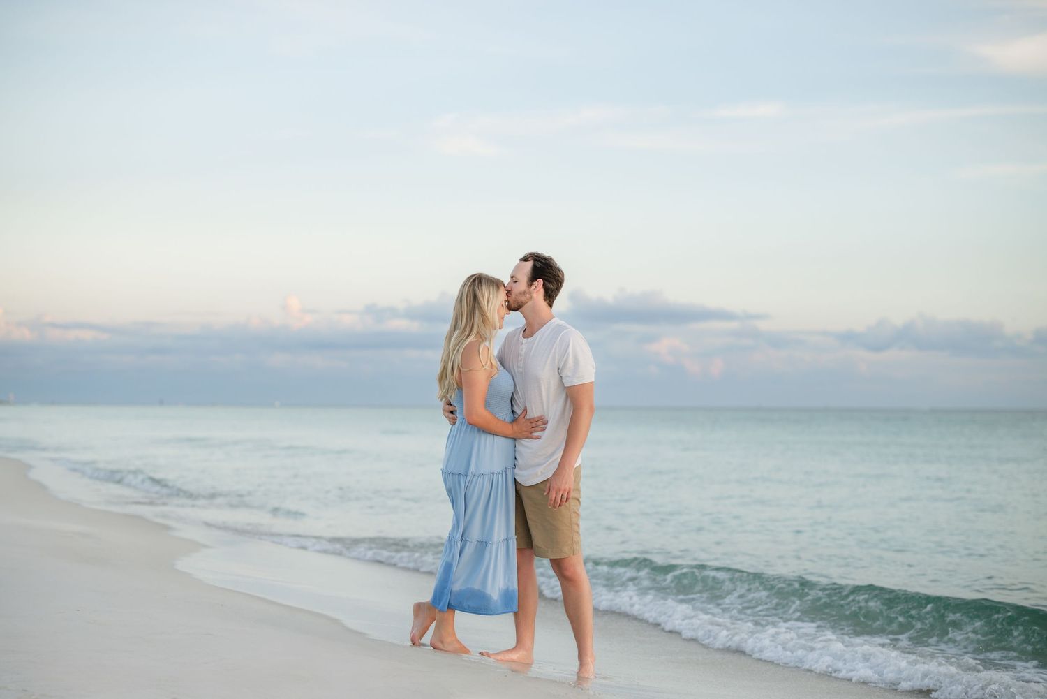 Romantic beach portraits with soft pastel sky and rolling waves in the background.