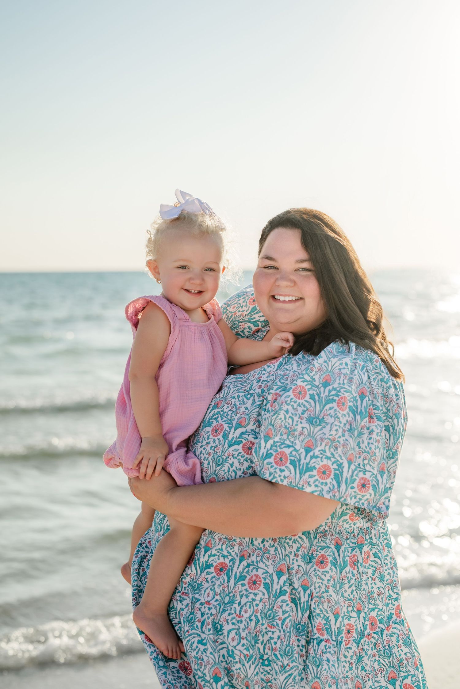 A mother and young child share a joyful moment together on a sunny beach.