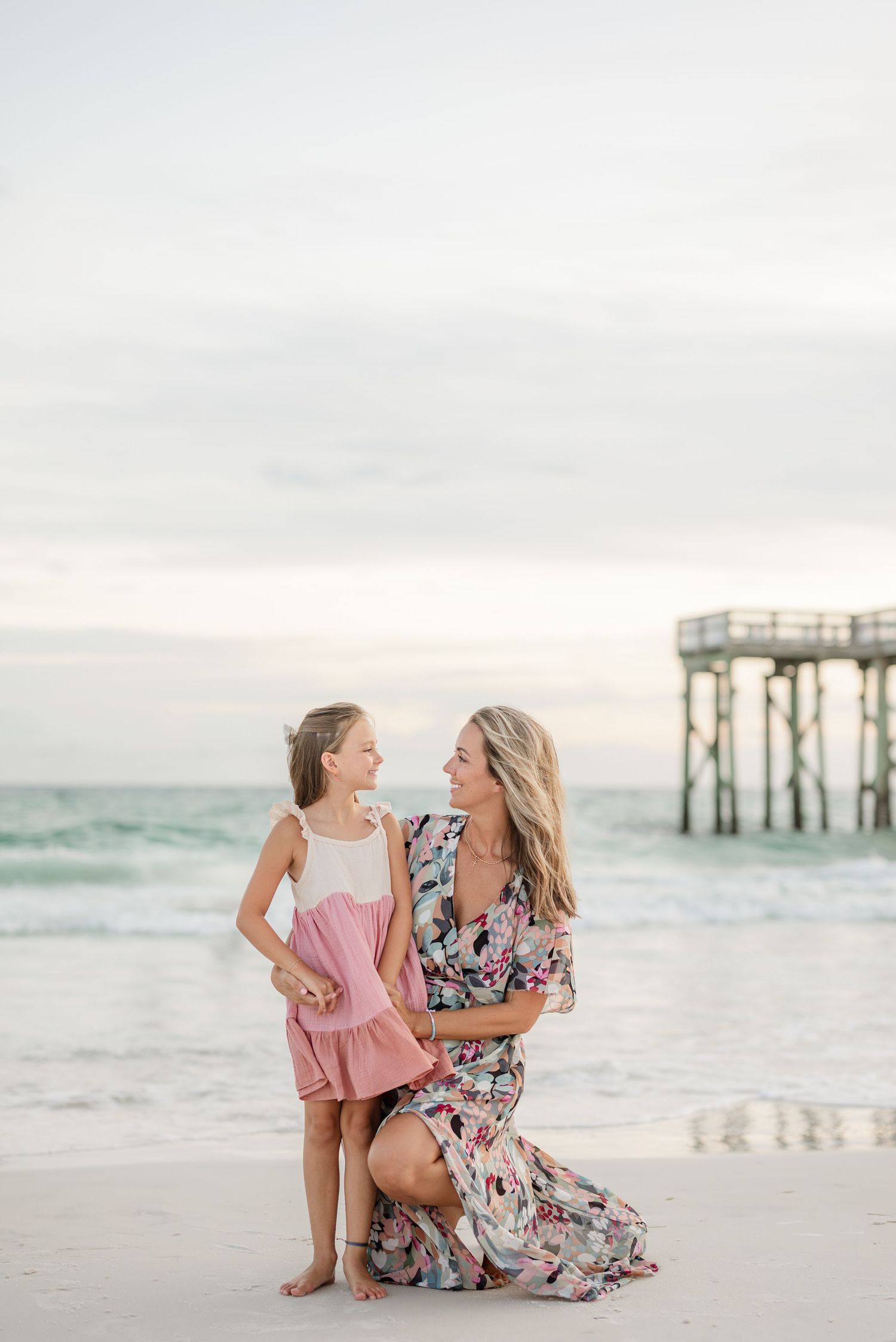 Mother and daughter play together near a pier on a serene beach at sunset.