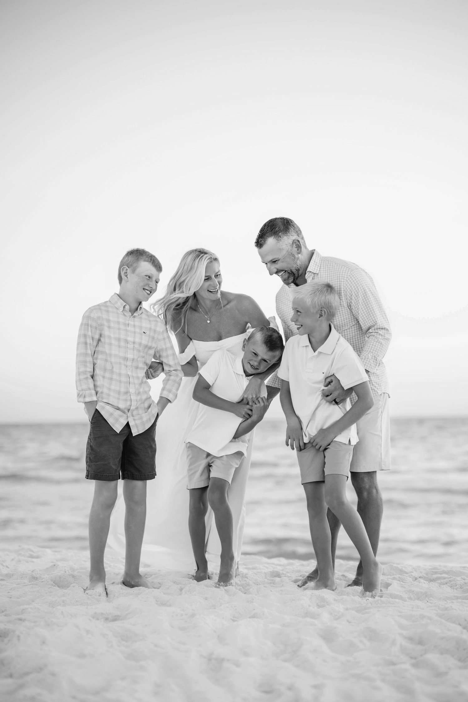 Group of people bending down to examine something interesting in the white sand on a beach.