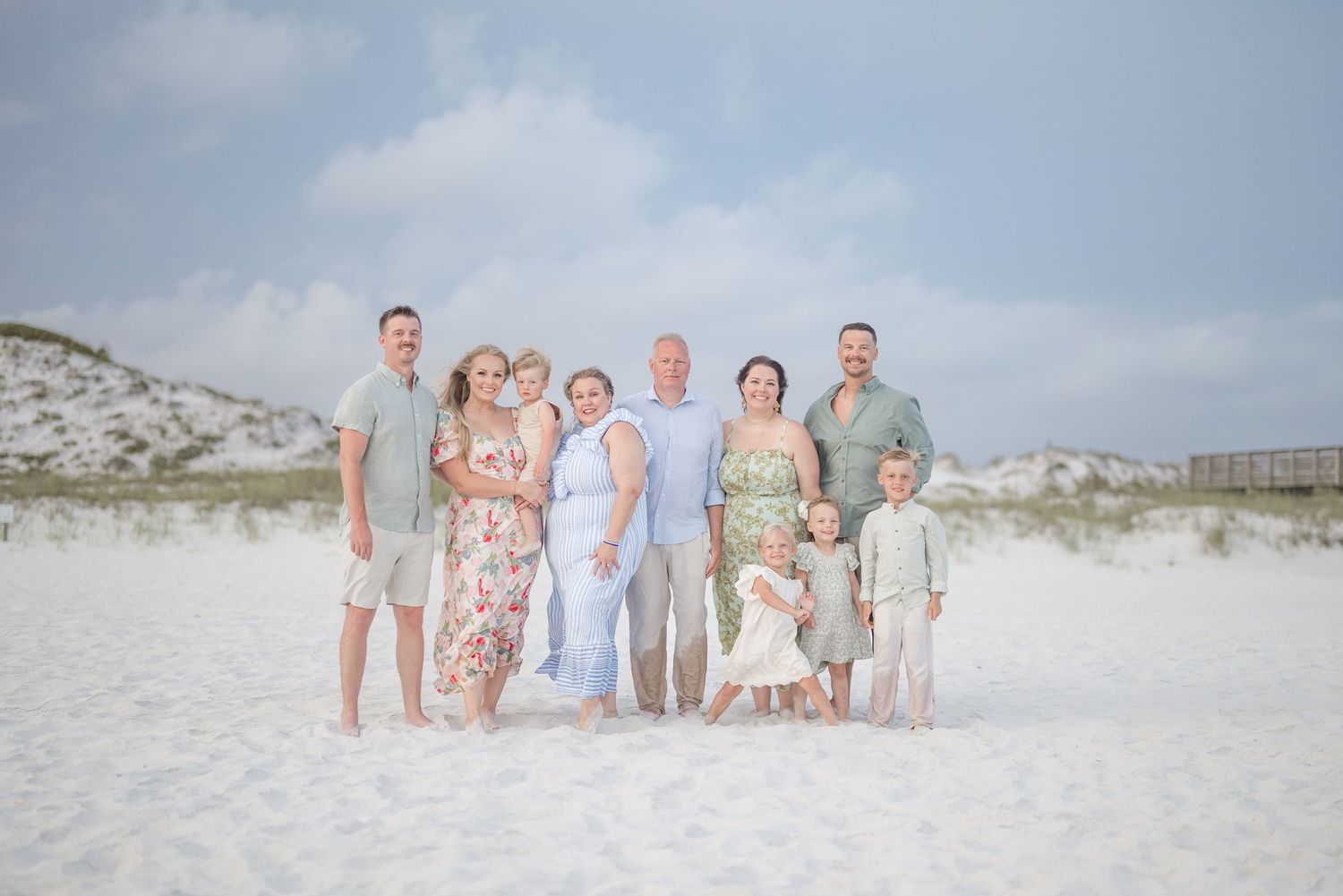 Large family group photo on pristine white sand beach with wooden pier in distance.