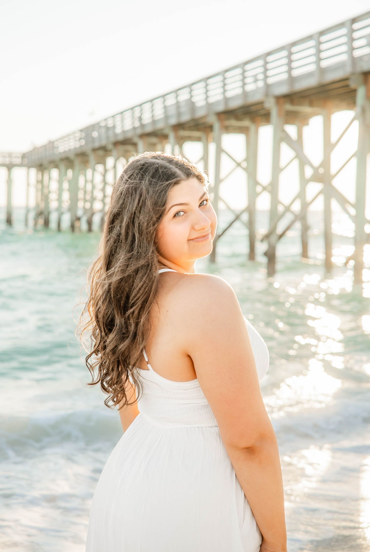 Ethereal beachside portrait session with turquoise waves and a wooden pier in the background.