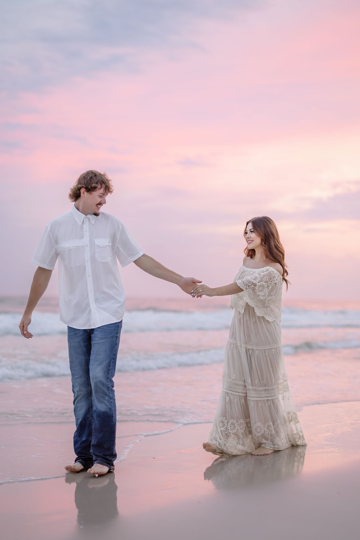 Couple dances playfully along the shoreline during pink sunset at the beach.