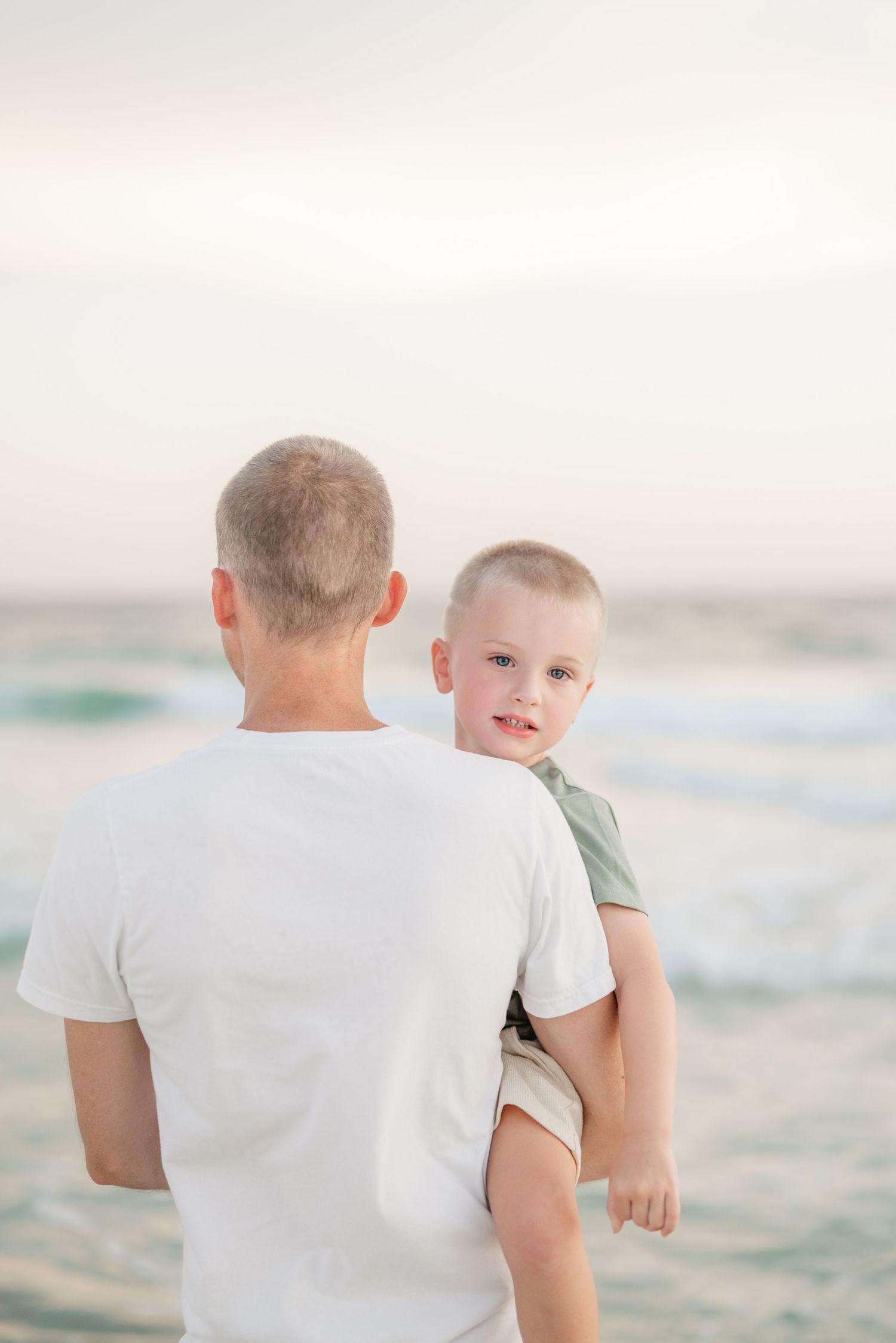 Parent and child looking out at ocean waves during sunset.