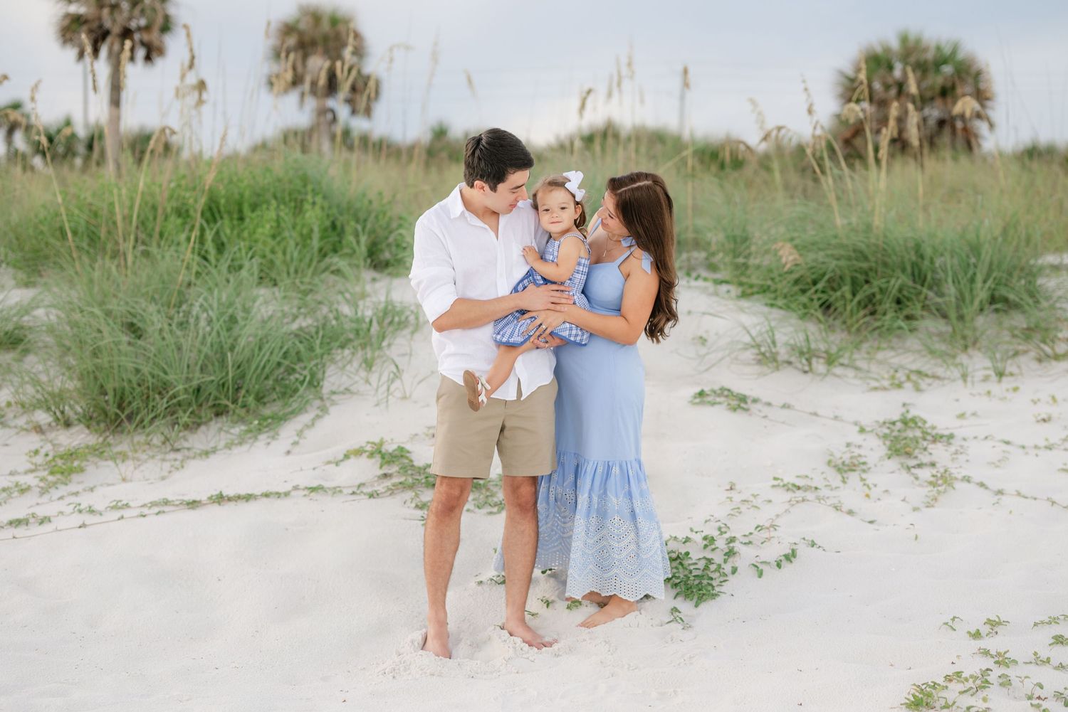 Family walking together along coastal dunes with sea oats and palm trees.