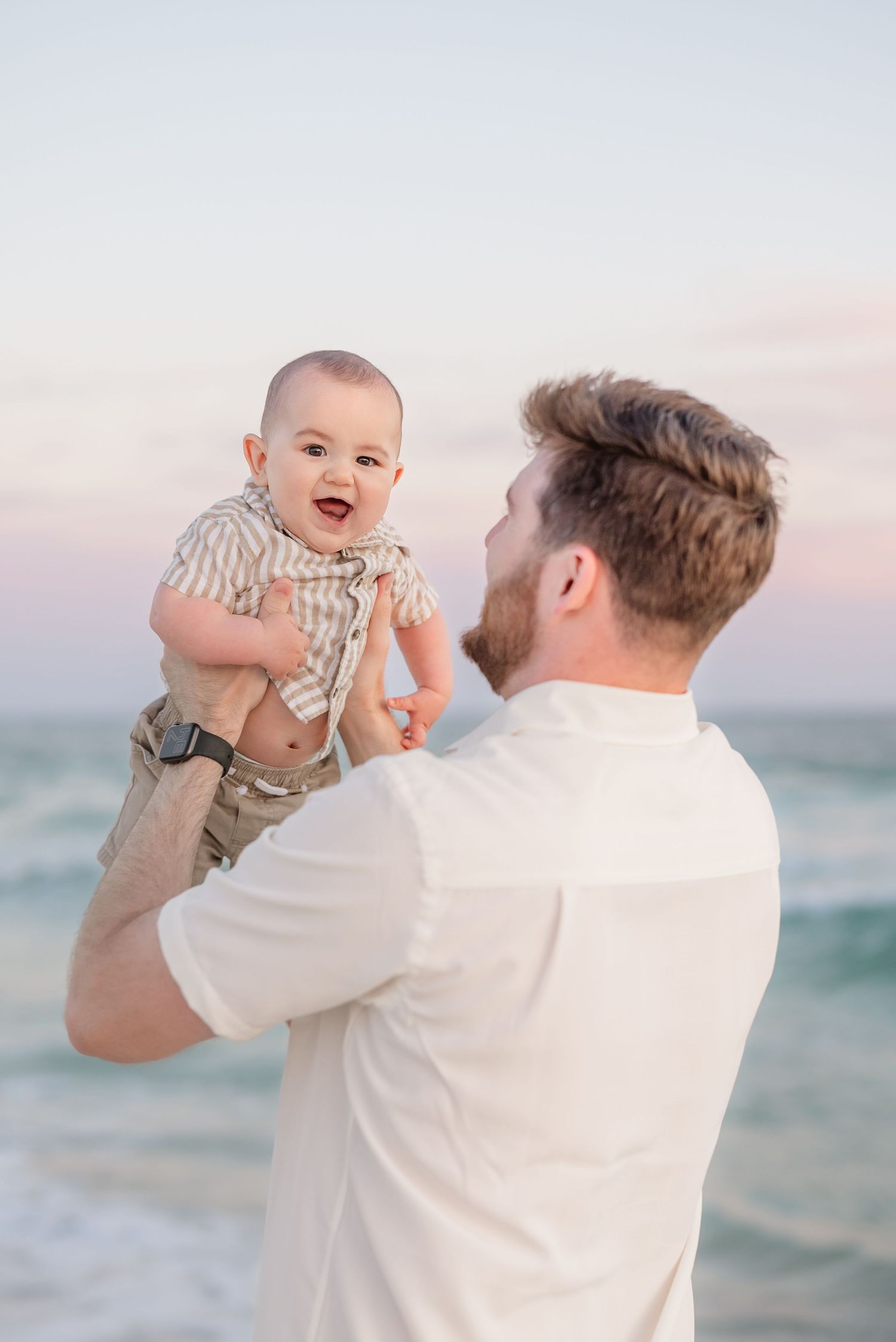 Playful interaction with a baby against ocean backdrop during golden hour.