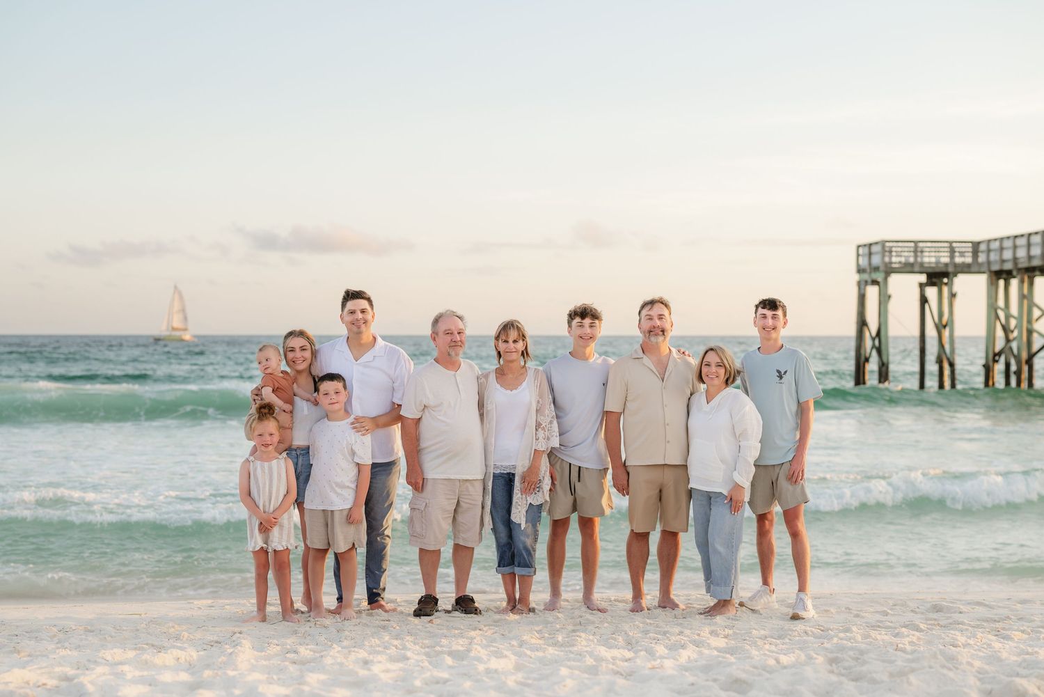 Extended family group photo on beach with ocean and sailboat in background.