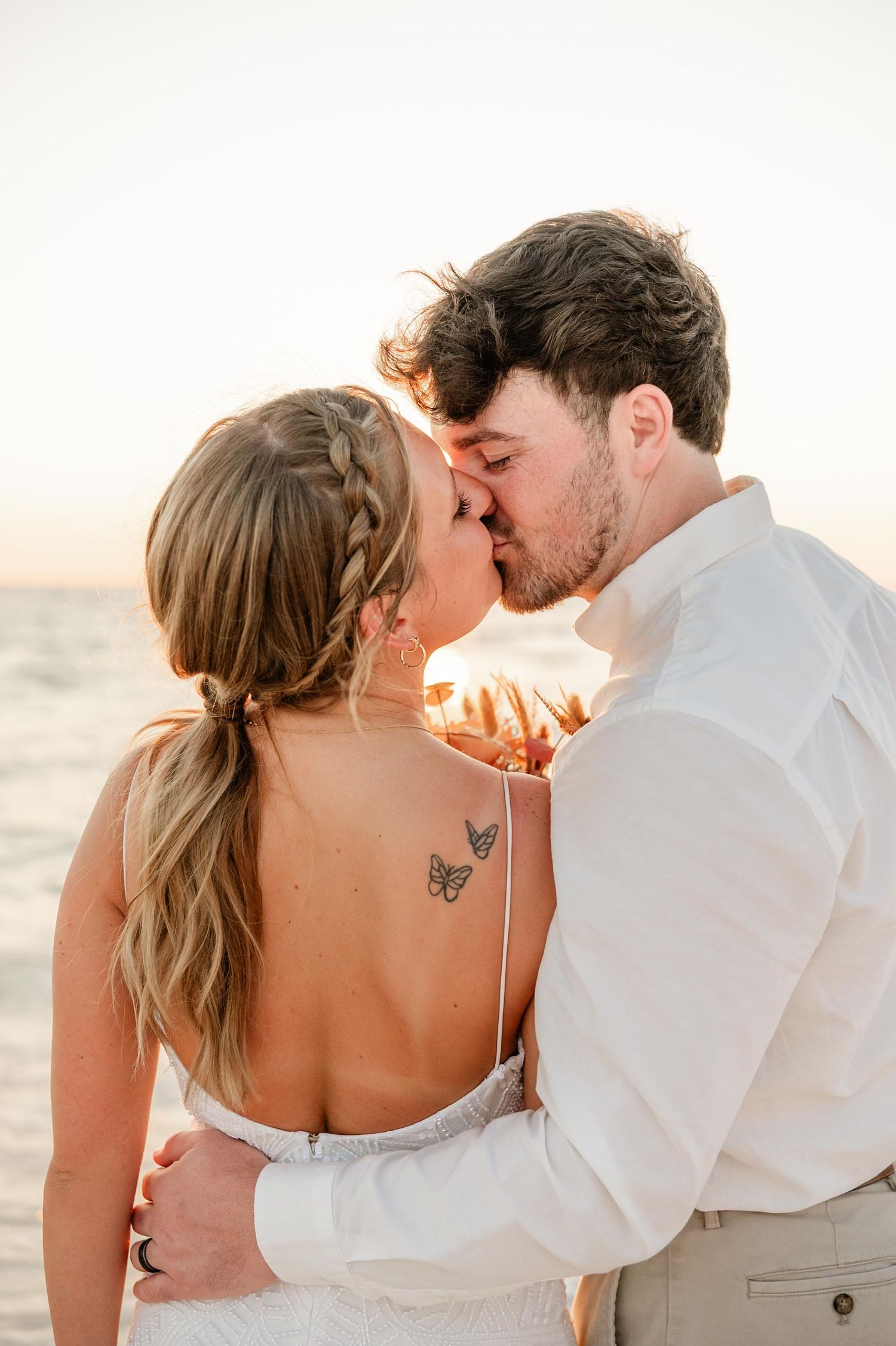 A romantic sunset beach wedding moment captured with a couple sharing an intimate kiss.