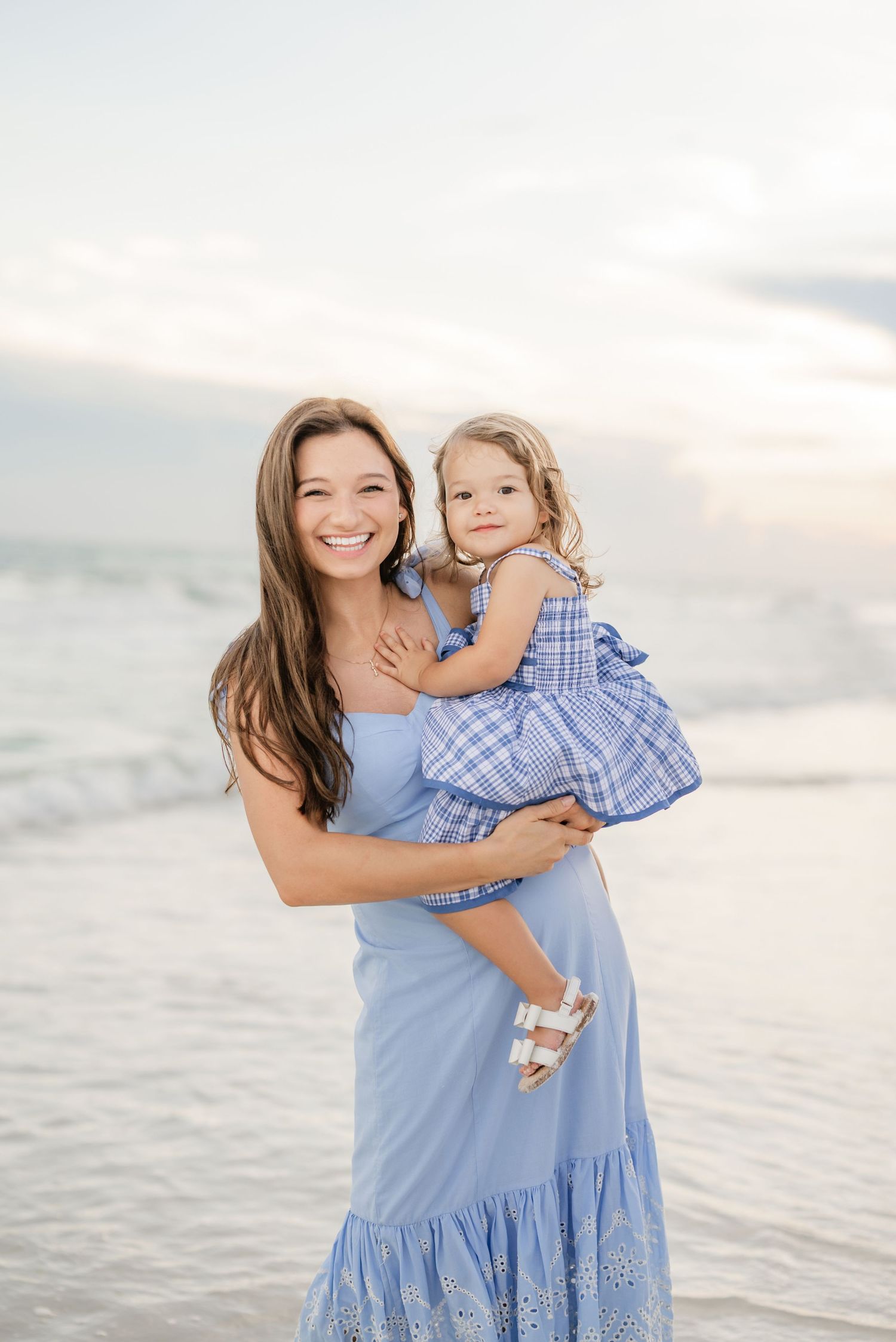 Mother and child in matching blue outfits sharing joyful moments on beach at sunset.