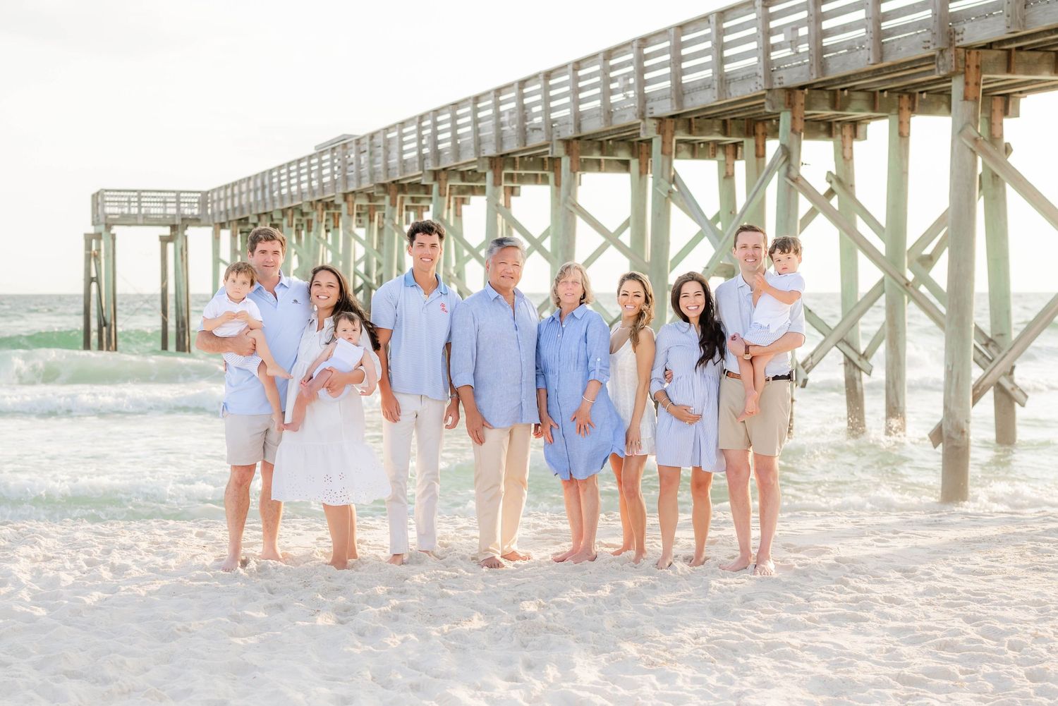 Multiple families gathered for beach portraits near wooden pier at sunset.