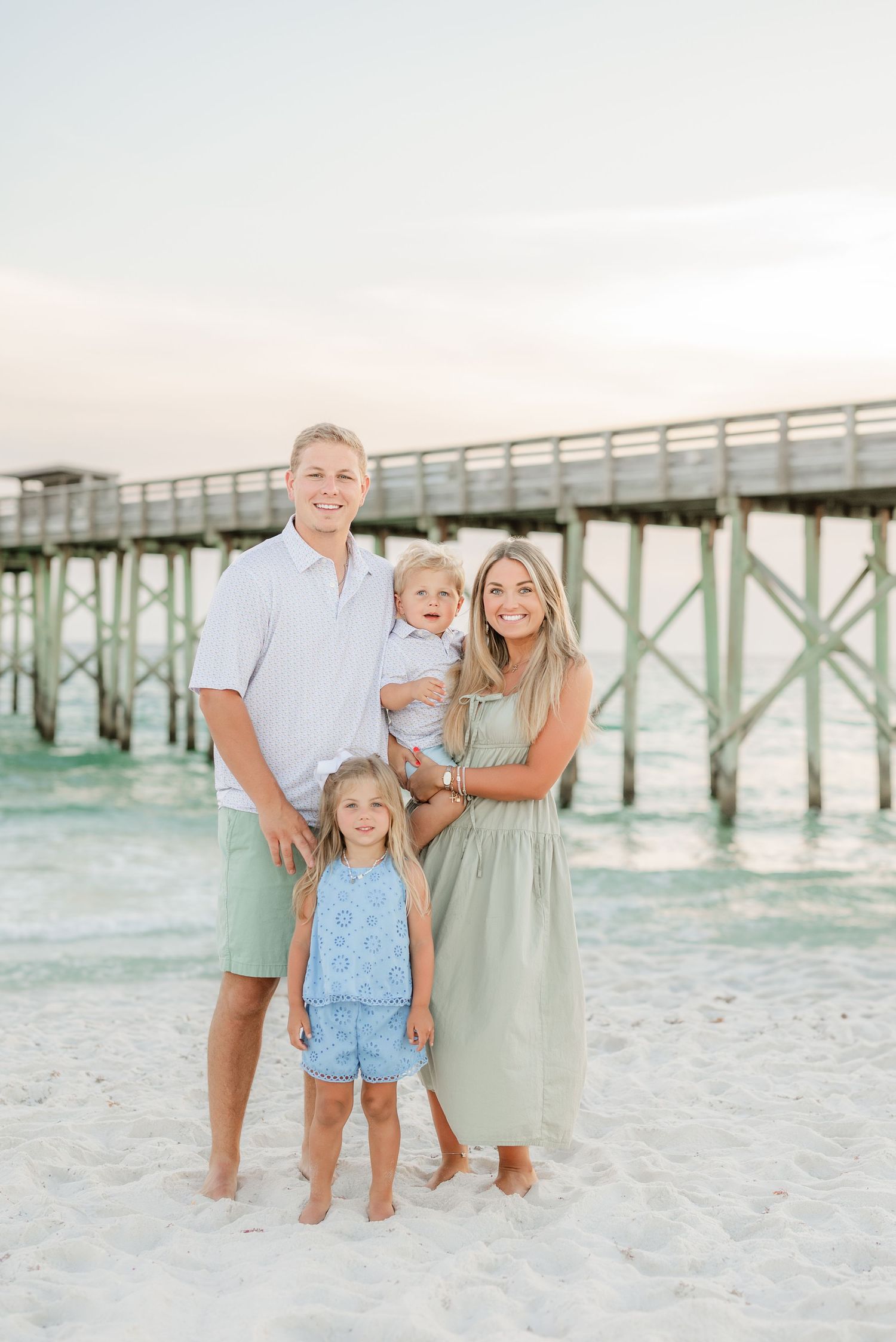 Family portrait session on beach with wooden pier and gentle waves in background.