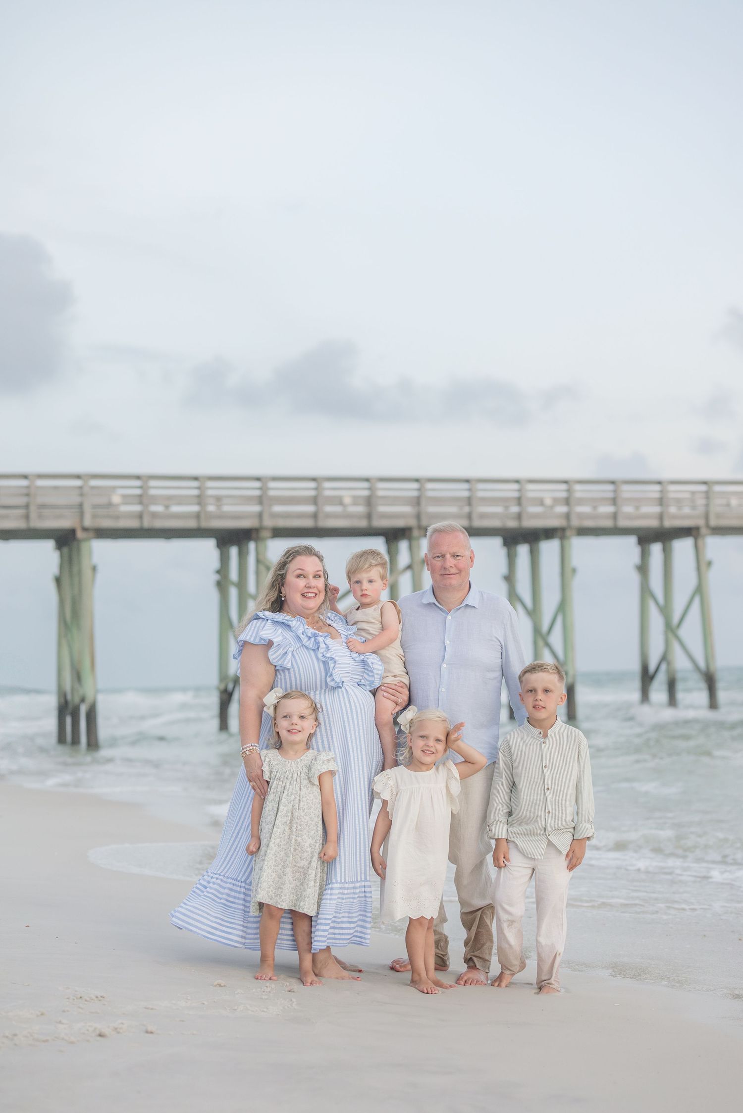 Extended family portrait session on a white sandy beach with a wooden pier in the background.