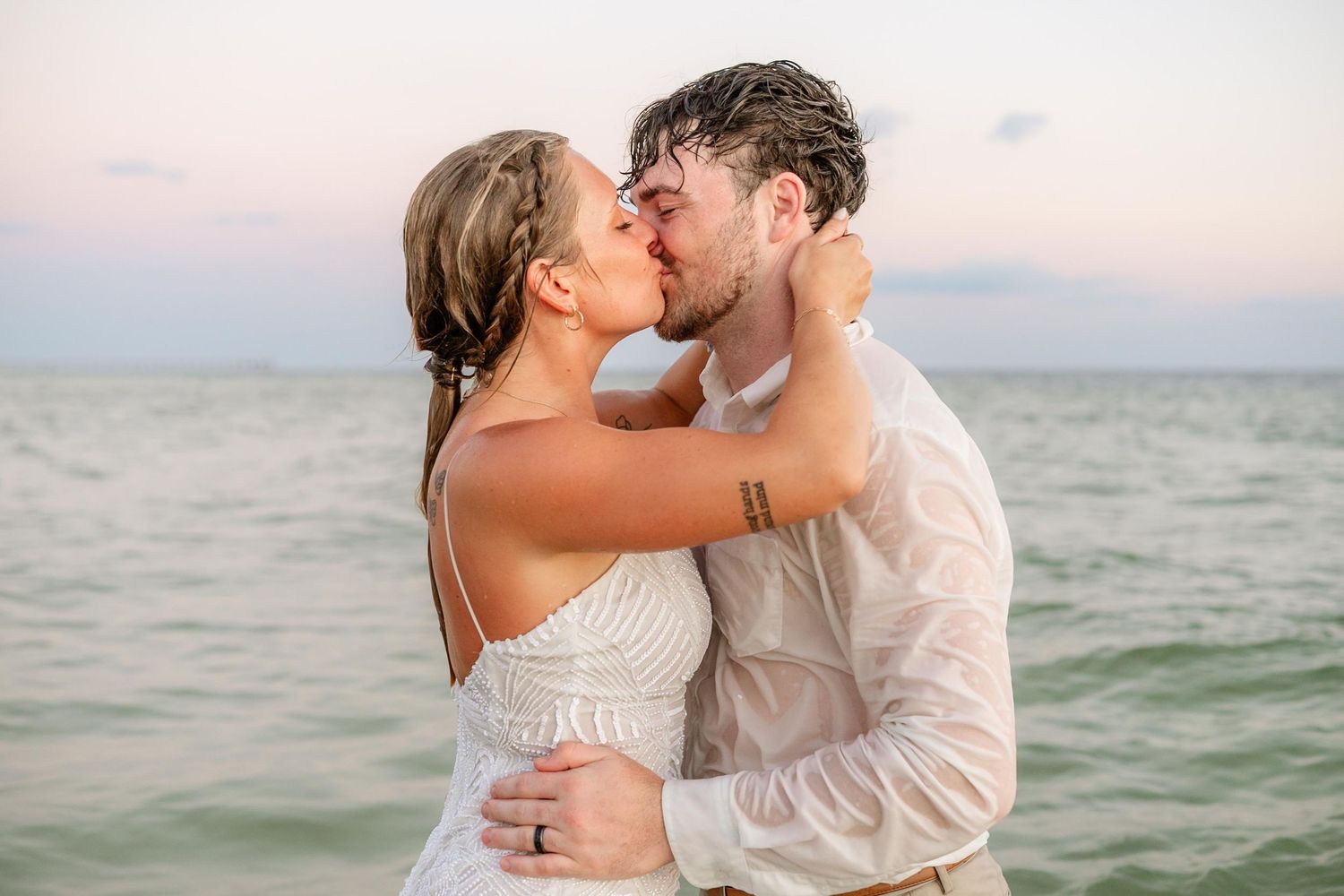 Newlyweds kiss passionately during beach photoshoot in gentle ocean waves.