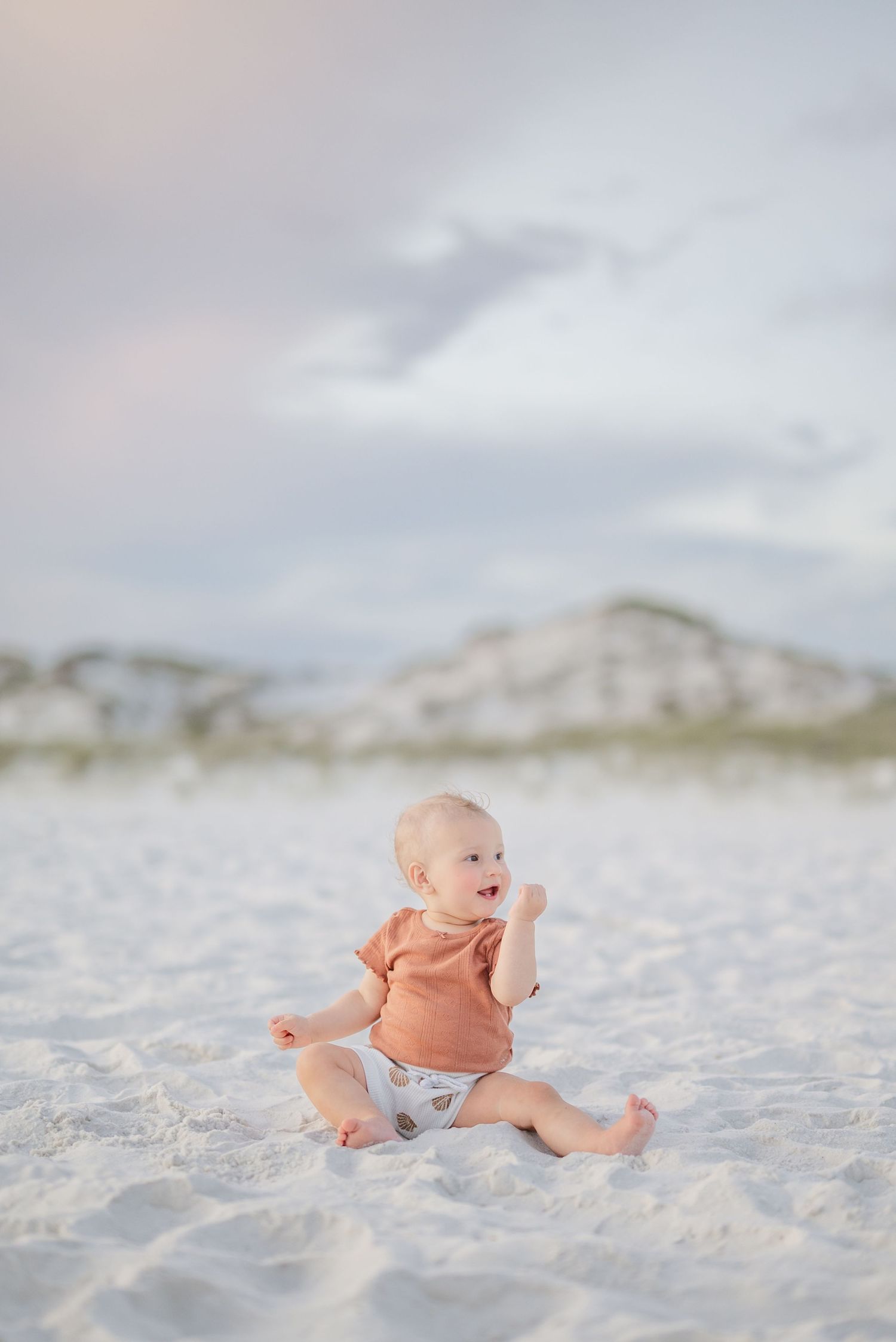 Infant in coral colored outfit crawling on soft white beach sand in Panama City Beach, Fl..