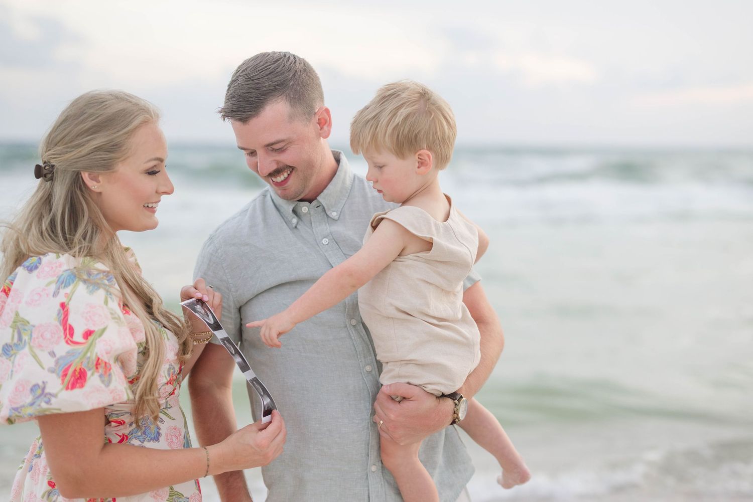A family shares an intimate moment on the beach while looking at ultrasound photos.
