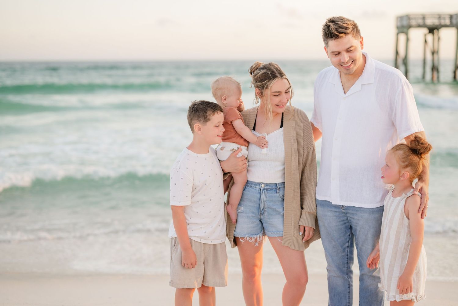 Casual family beach portraits with soft pastel colors and ocean waves in background.