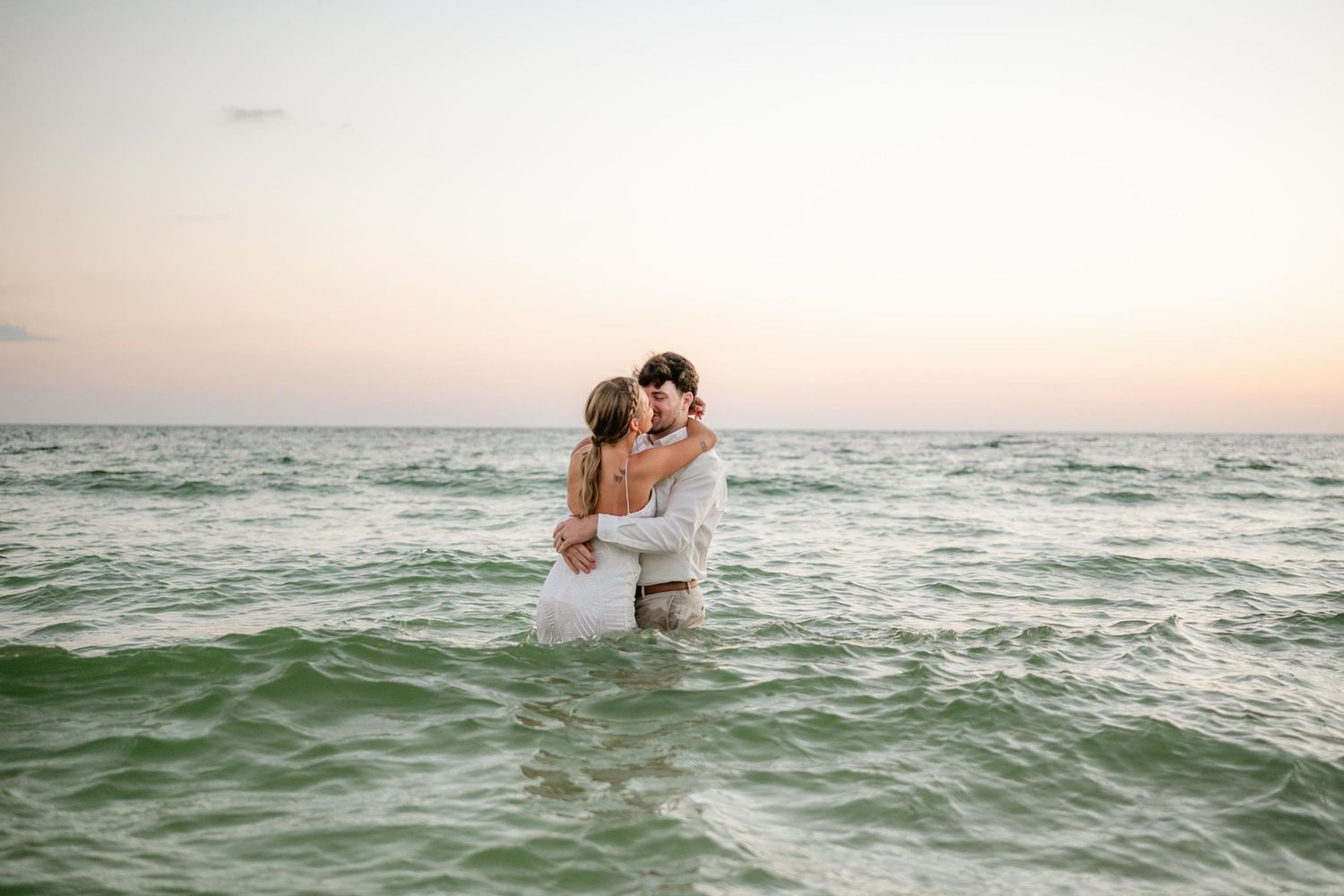 Romantic couple embraces in gentle ocean waves during sunset.
