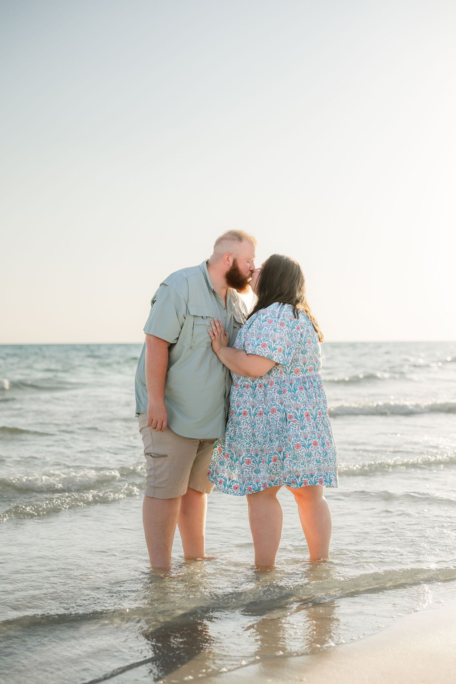 Romantic beach photoshoot with couple wading in shallow ocean water during golden hour.