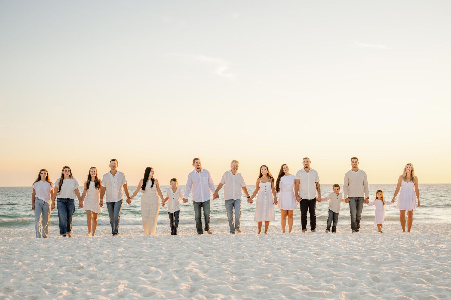 Extended family members holding hands in a line along pristine white sand beach at dusk.