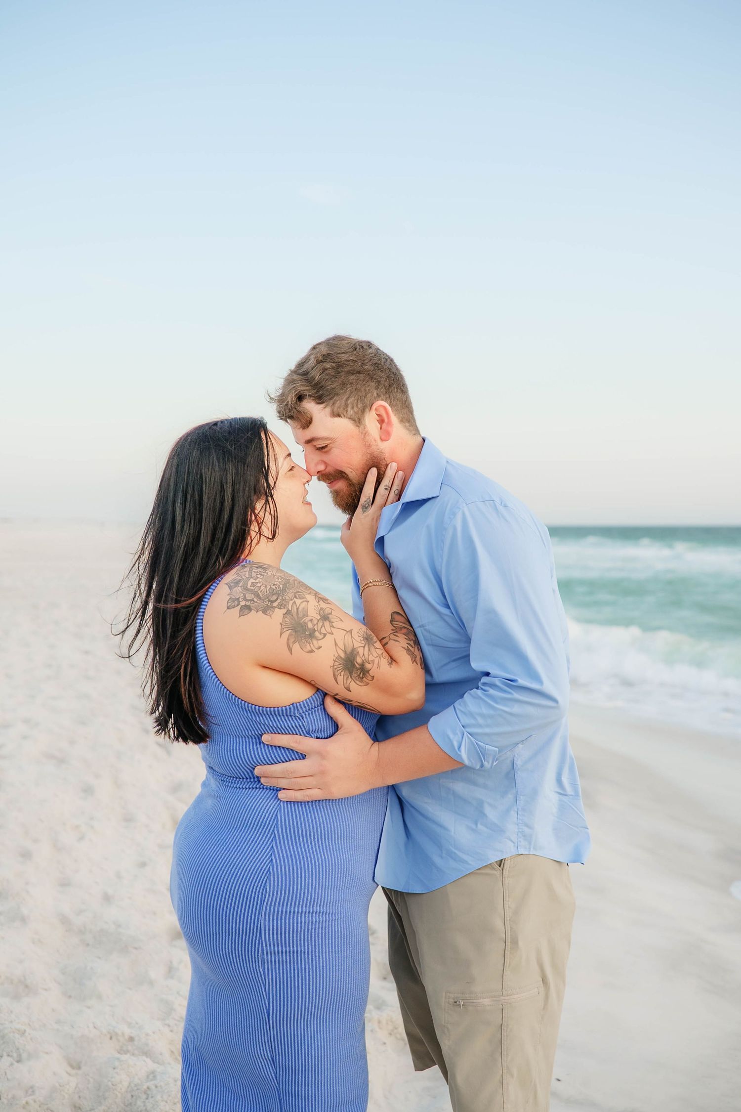 A romantic beach photoshoot showing a couple embracing on white sand with ocean waves in the background.