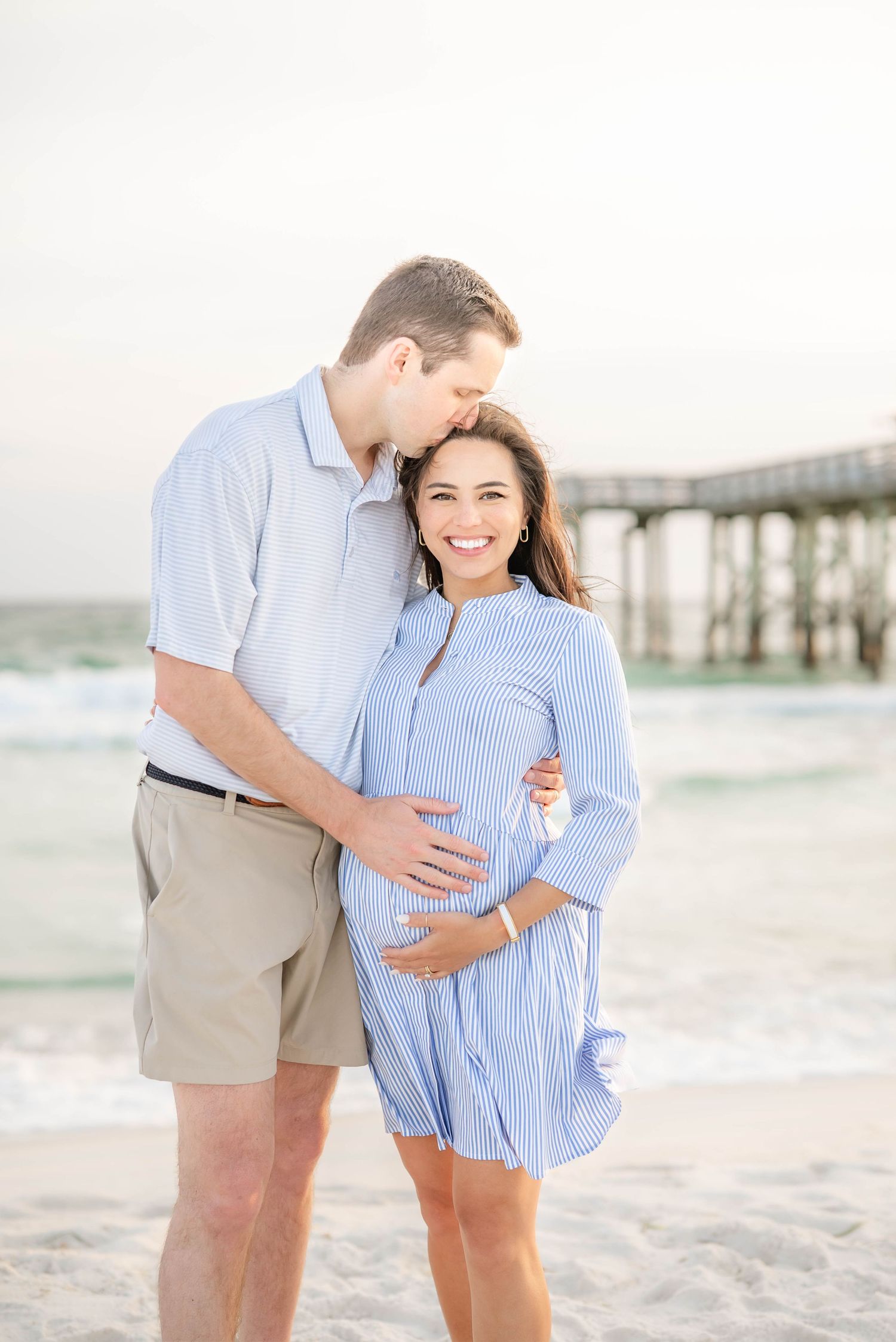 A couple shares an intimate moment during their maternity photoshoot on the beach.