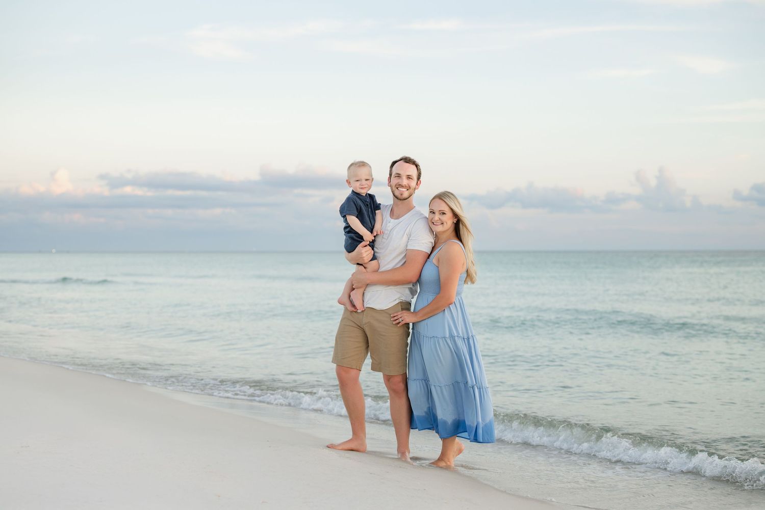 Family walking together along a scenic beach shoreline at sunset with gentle waves in the background.